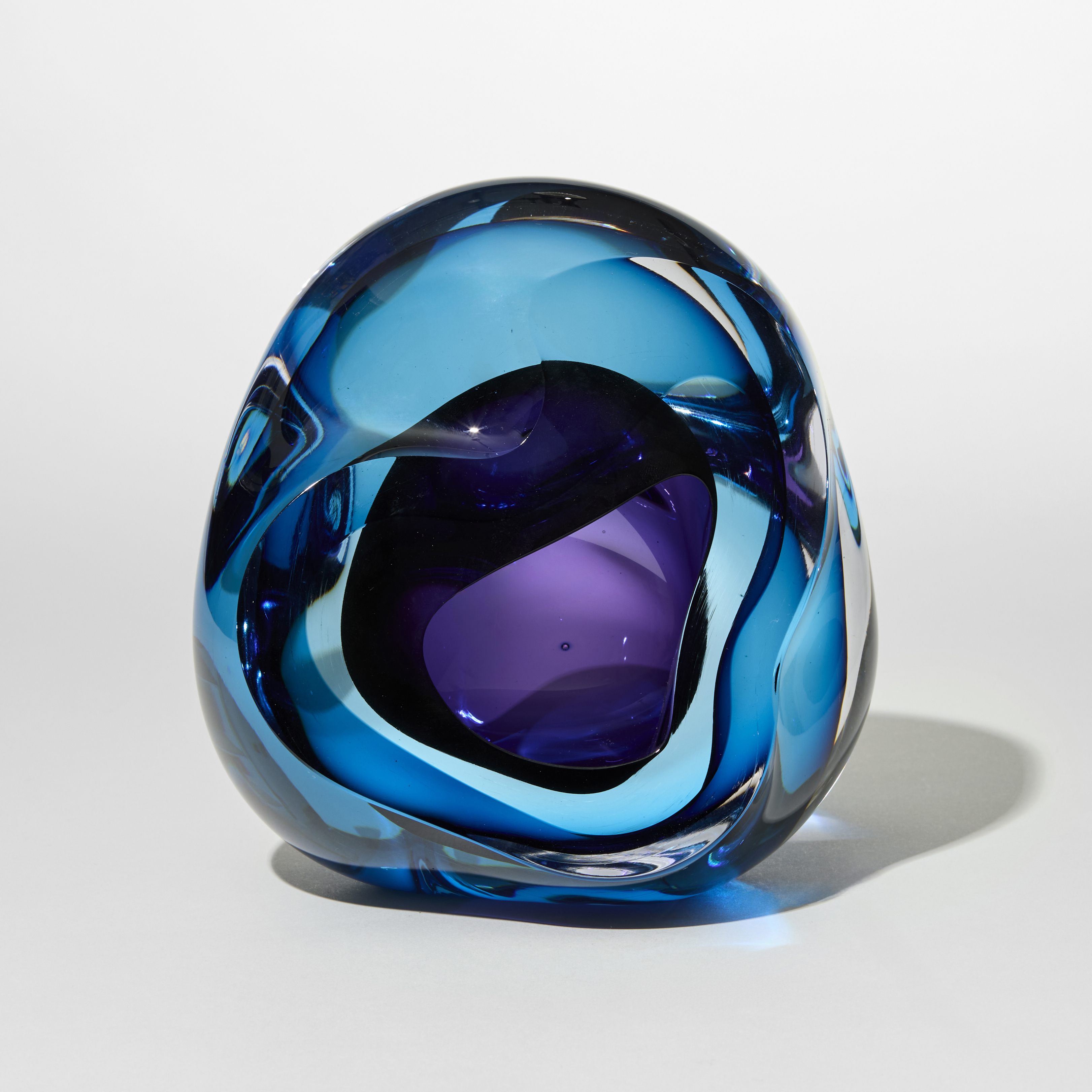 transparent soft rock form with merging layers in clear blue and purple and a central hole with the opening from the front hand made from blown and sculpted glass