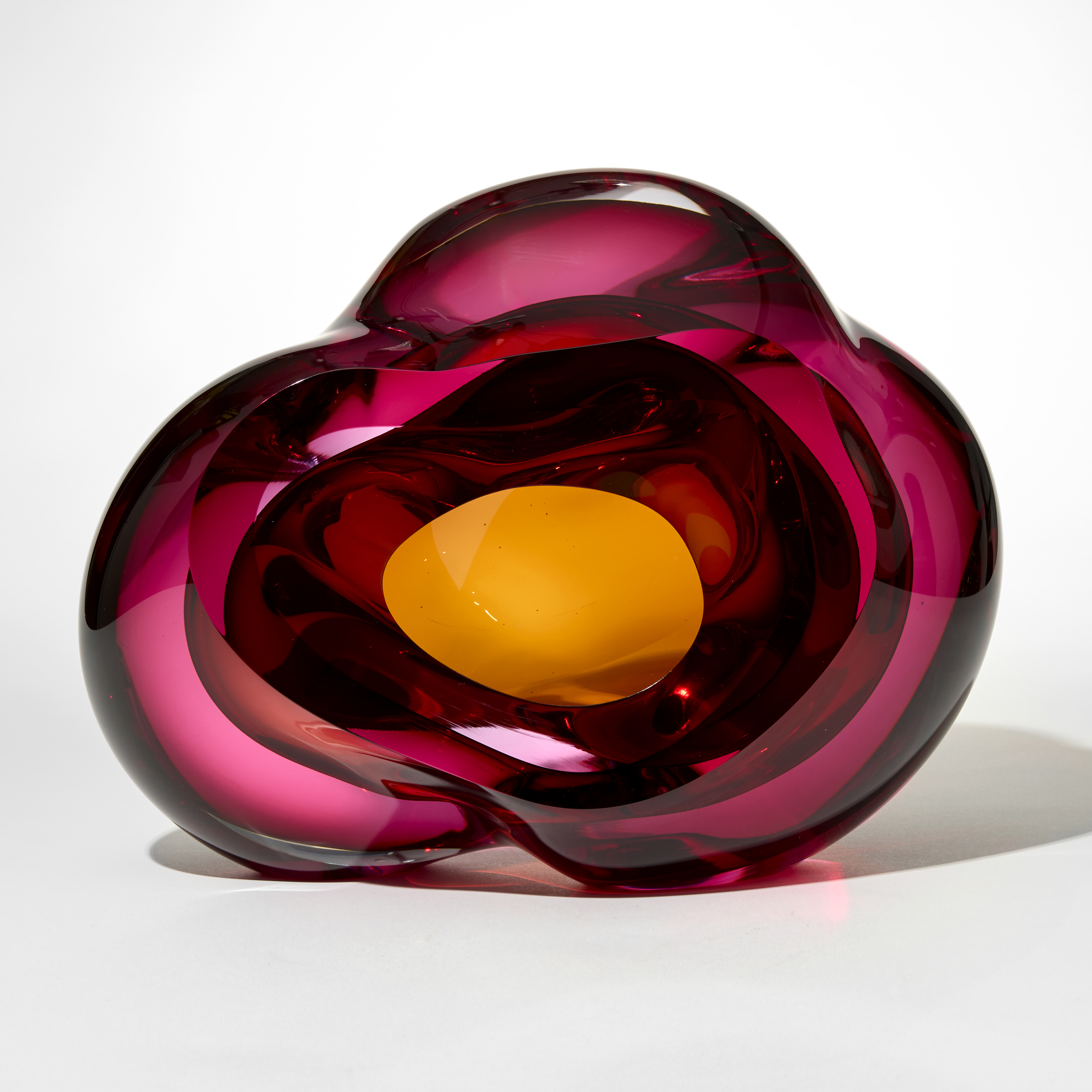 transparent cloud like form with merging layers in clear cerise pink and yellow gold inspired by geodes with a central opening and inner cavity exposed from the front hand made from blown and sculpted glass