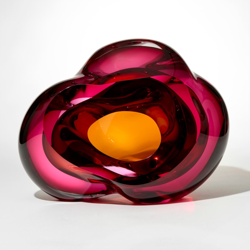 transparent cloud like form with merging layers in clear cerise pink and yellow gold inspired by geodes with a central opening and inner cavity exposed from the front hand made from blown and sculpted glass