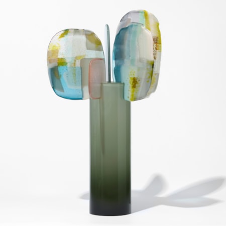 smokey shiny opaque teal cylinder with 5 different shaped and sized rounded petals perched on the top edge each with abstract surface patterns in blue white pink and mustard yellow hand made from blown and fused glass