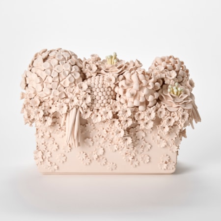 a monochromatic light pink ceramic sculpture resembling a dense floral arrangement featuring an ornate cluster of intricately sculpted flowers including hydrangea like blooms roses and textured spherical elements overflowing from the top of a rectangular base with smaller blossoms cascading down the sides giving the piece a highly detailed cake-like decorative appearance hand made from coloured porcelain