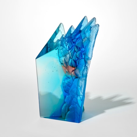tall angular transparent abstract jade blue and pink sculpture with two flat and polished sides and two inverted sides with craggy rock like textures hand made from cast glass