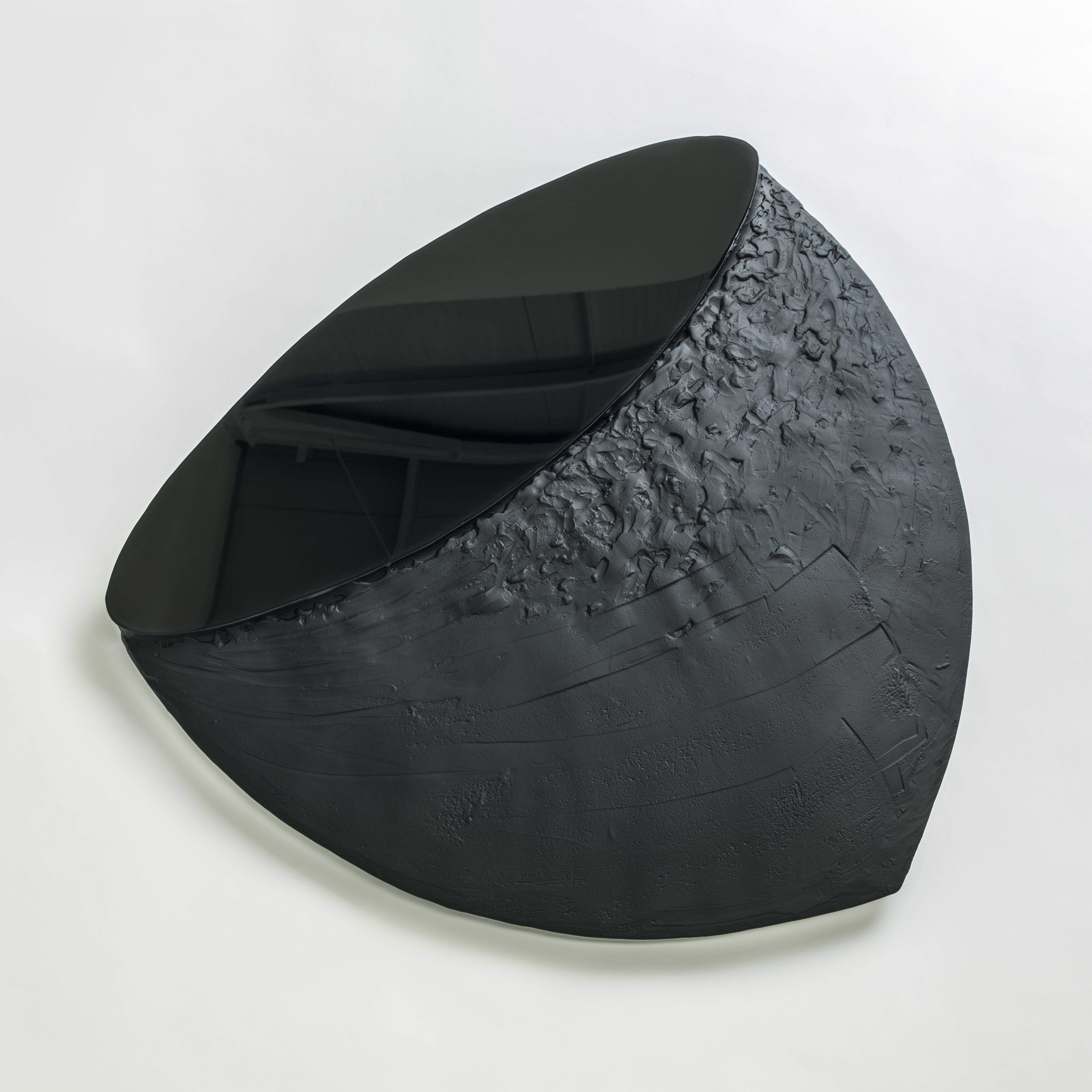 flat black blunt hazelnut shaped wall mounted artwork with upper oval shiny reflective disc area and lower matt organically textured area hand made from glass