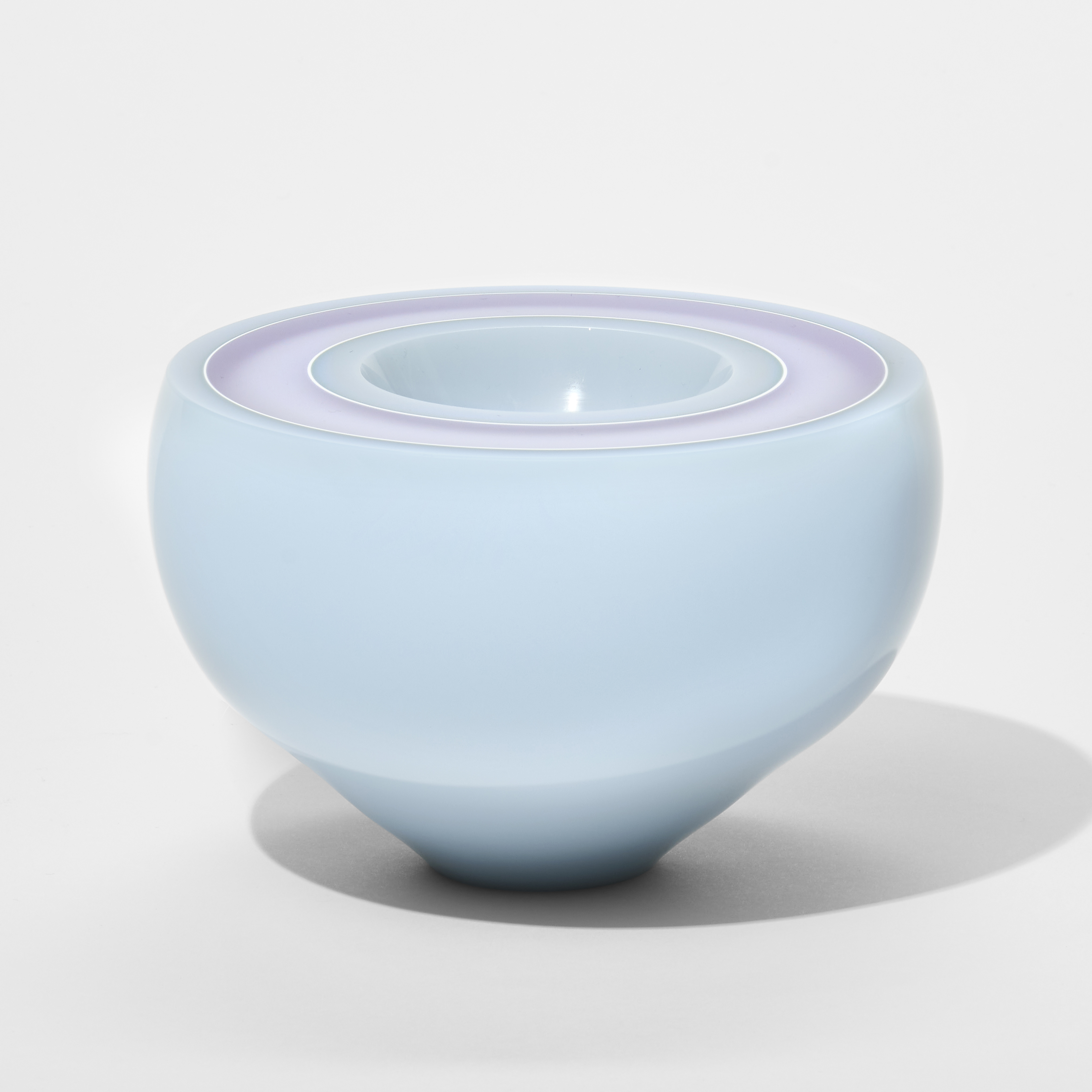 round low glossy opaque bowl in soft baby pale blue with a wide flat top edge with concentric rings in white pink and lilac and a wide central hollowed out hole hand made from glass 
