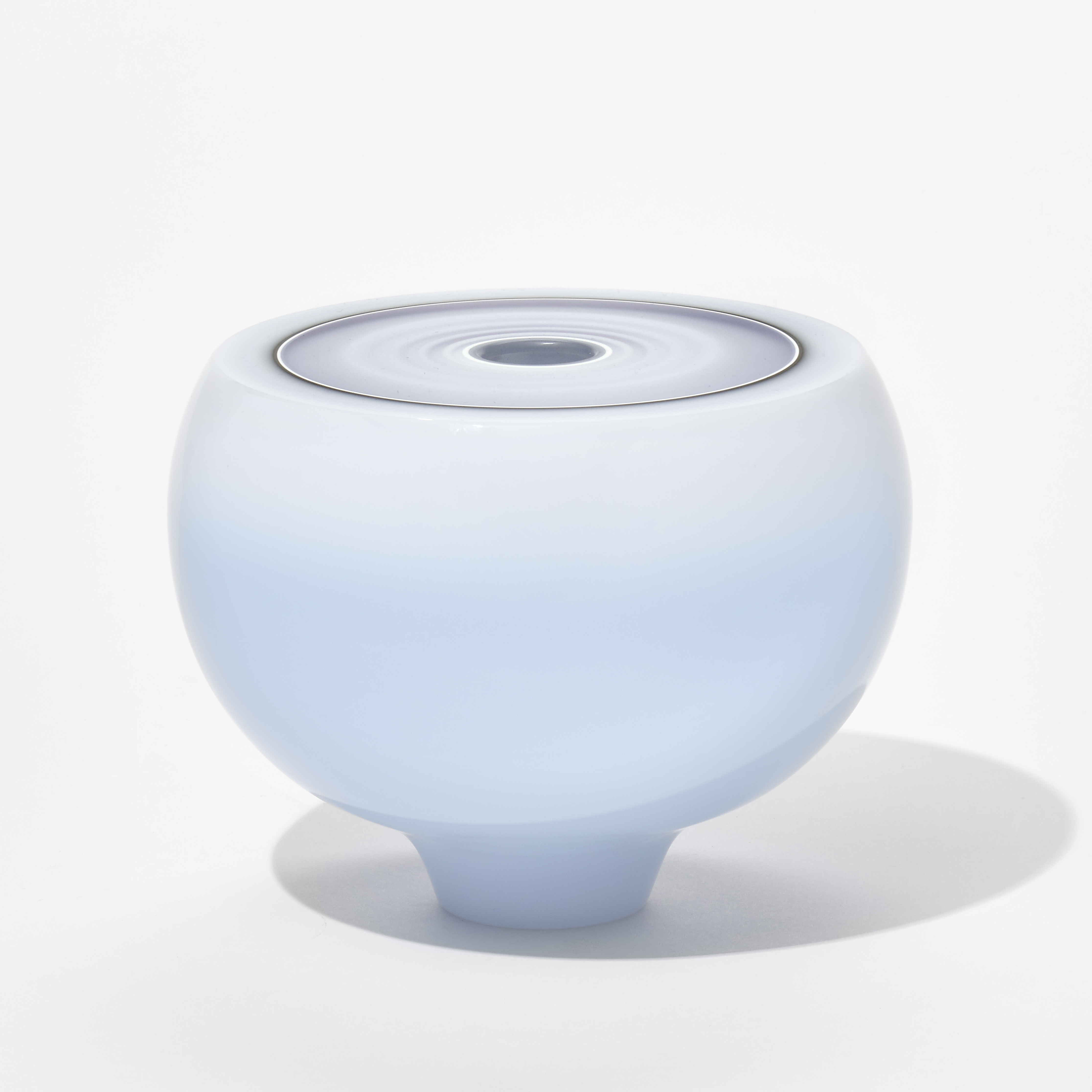 glossy round opaque white fading to very soft pale blue vessel with a narrow tapered foot and flat top surface with concentric rings of grey white and mauve and a small central hole hand blown from glass