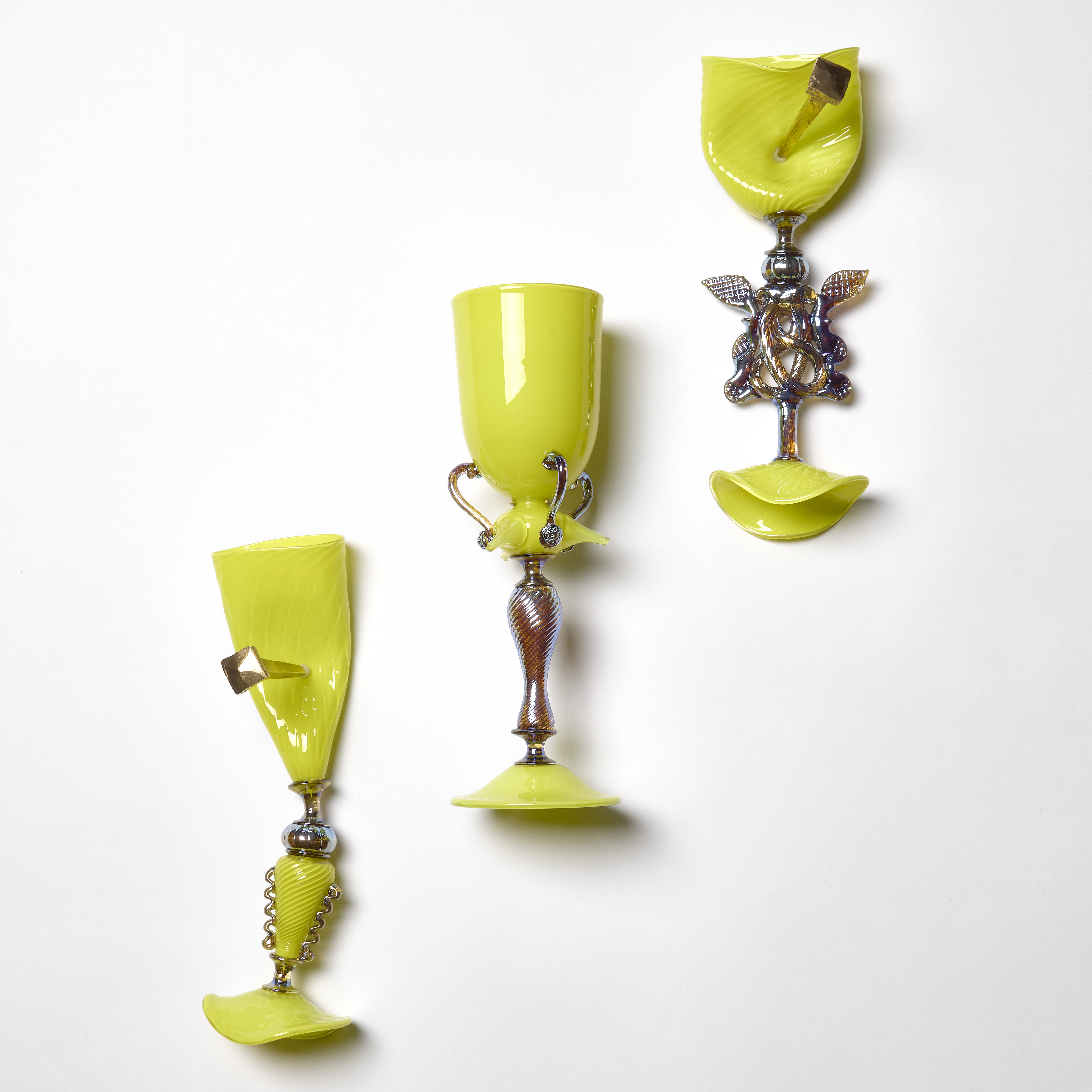 wall hanging sculptural series of three fluorescent yellow green goblets with the middle one perfect and held by an elegant fitting and the outer two distorted and nailed in place with two oversized bronze nails hand made from sculpted glass