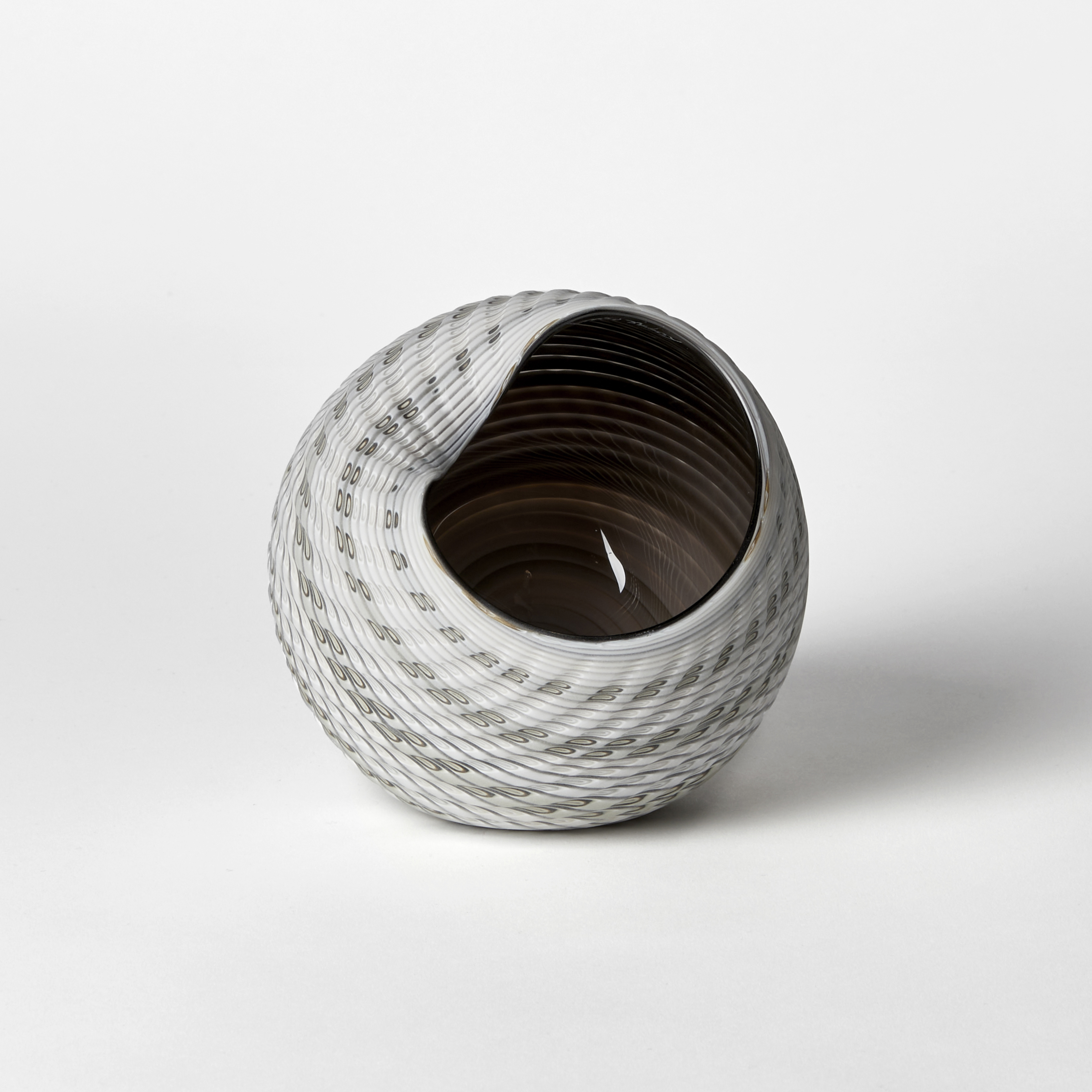 abstract round shell like vessel with matt exterior with incised cut surface in bands of white light grey blue and bronze with glossy interior hand made from glass