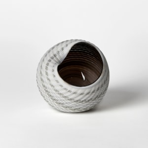 abstract round shell like vessel with matt exterior with incised cut surface in bands of white light grey blue and bronze with glossy interior hand made from glass