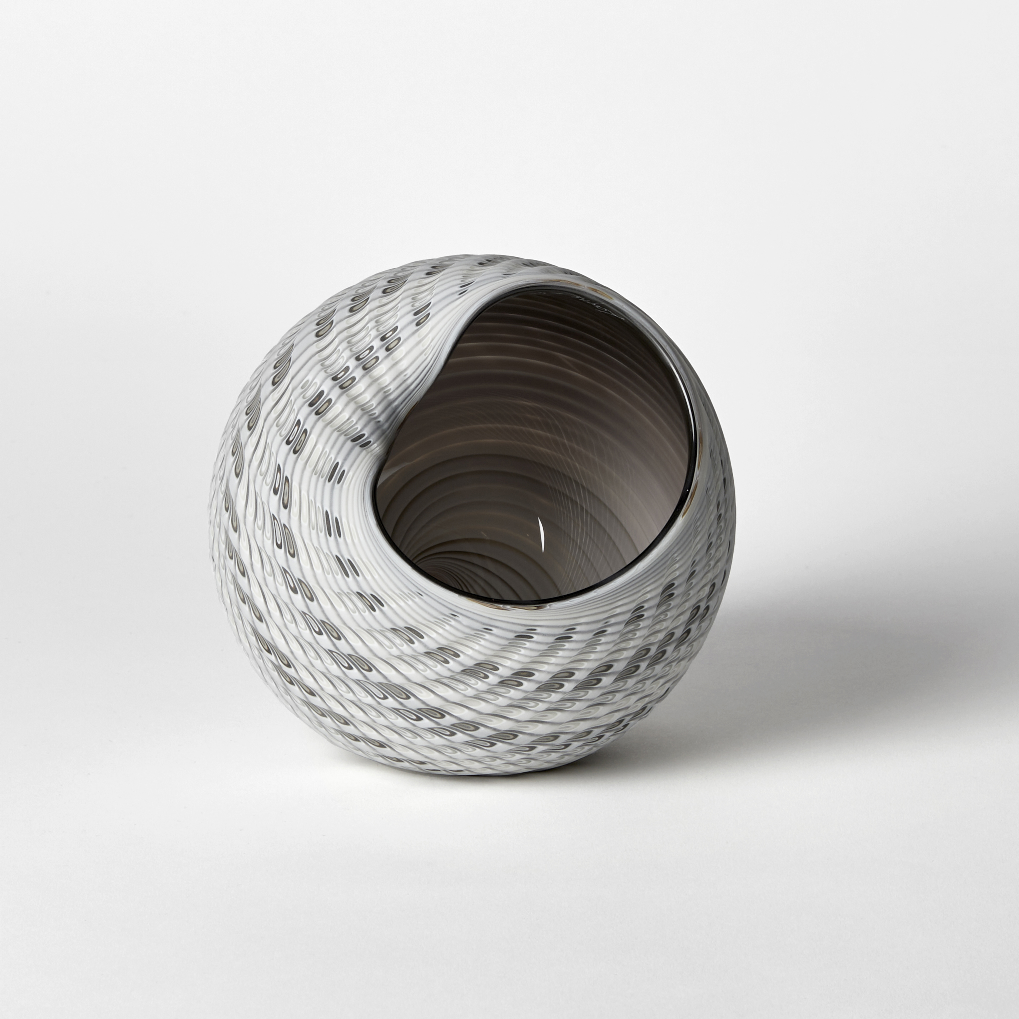 round shell like vessel with exterior matt textured cut surface in bands of grey light blue fawn and bronze with glossy interior hand made from glass