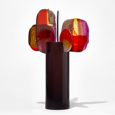 glossy dark chocolate cylinder with five rounded finials of glass perched on the top edge each with abstract patterns in bright red soft yellow purple and deep pink hand made from blown and fused glass