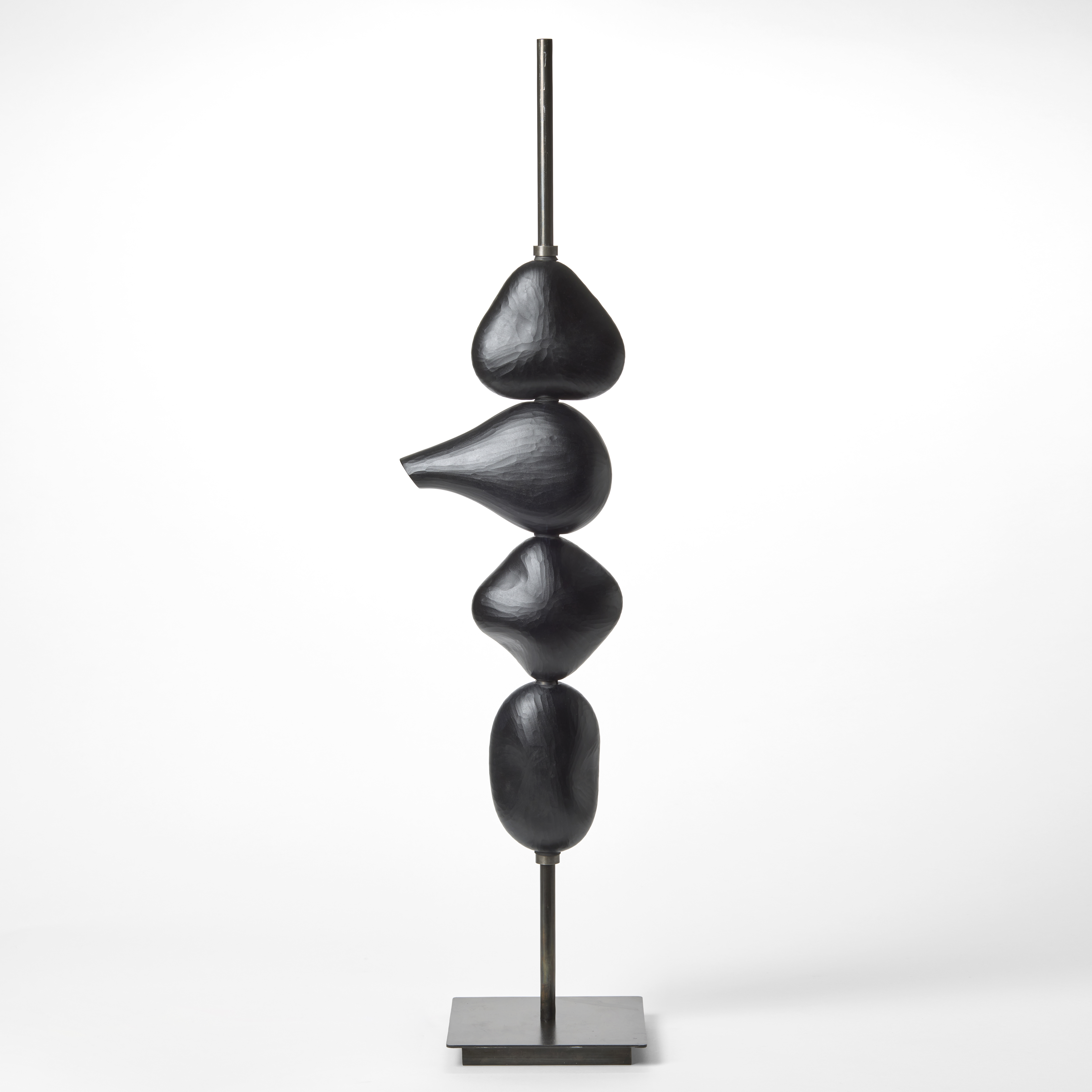 tall stacked sculptural light consisting of four abstract black shapes held on a long steel pole with a square base each with a LED light inside hand blown from glass with a textured cut surface