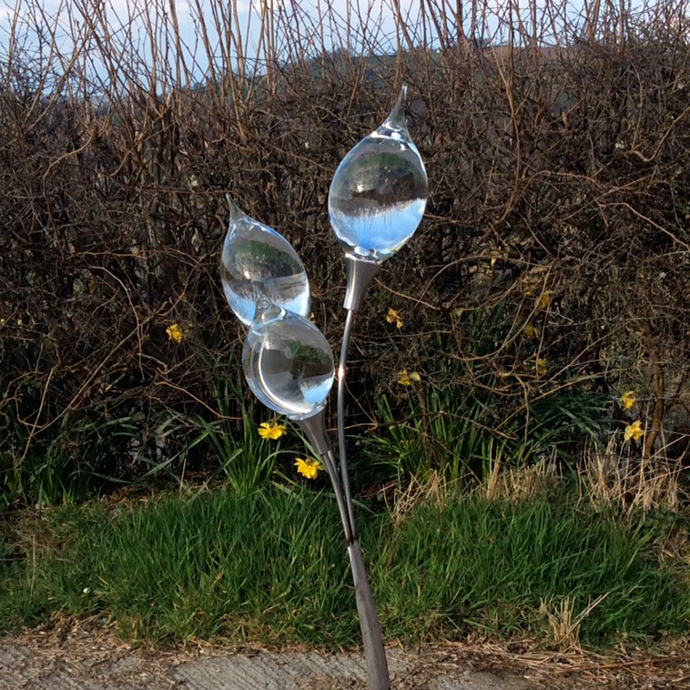glass art in the shape of a lamp on steel base pictured outdoors