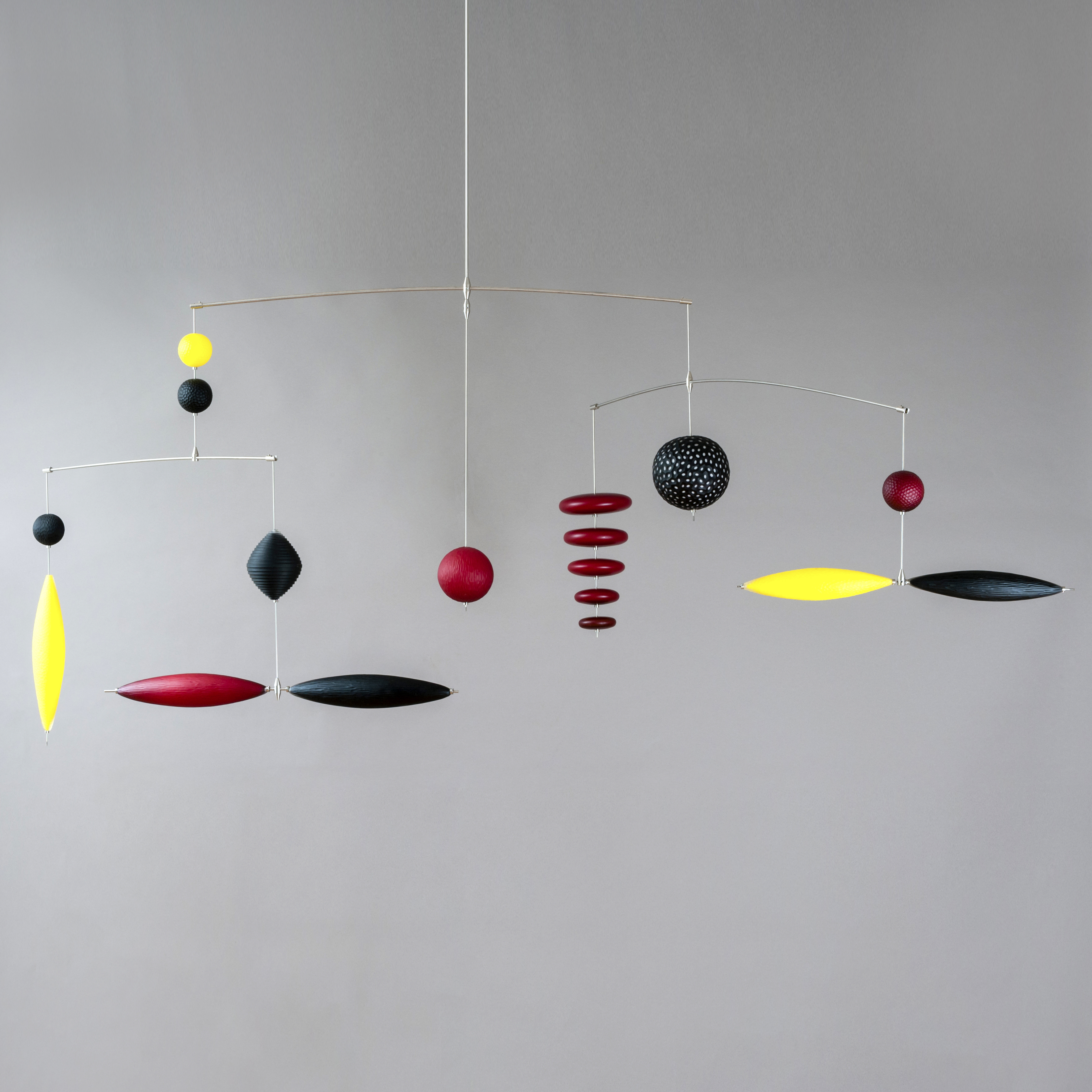 hanging mobile with suspended opaque shapes in black red and yellow in discs spheres and lozenges hand made from blown glass