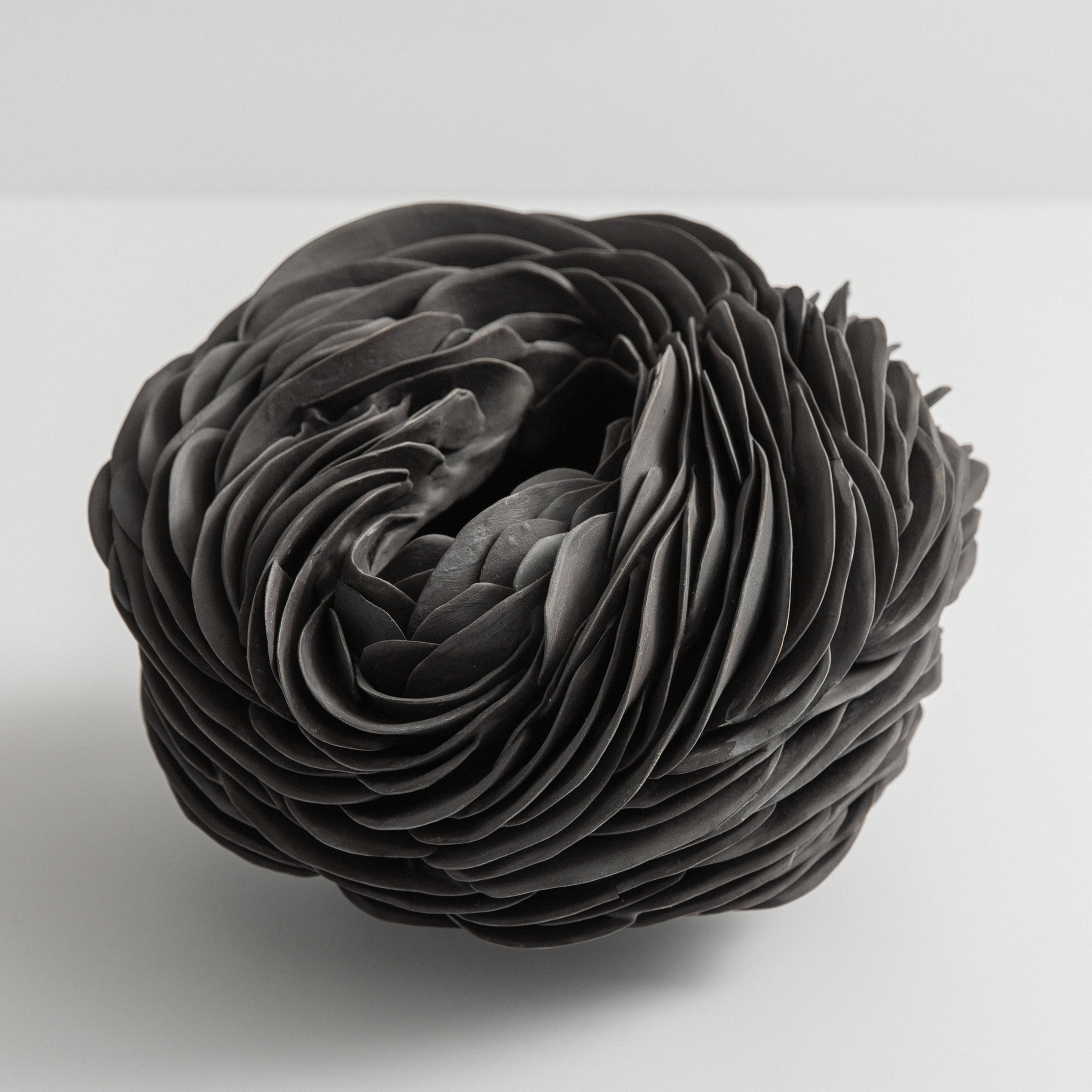low organic round form with slit top opening and the entire exterior covered in curved interwoven shards hand made from black porcelain
