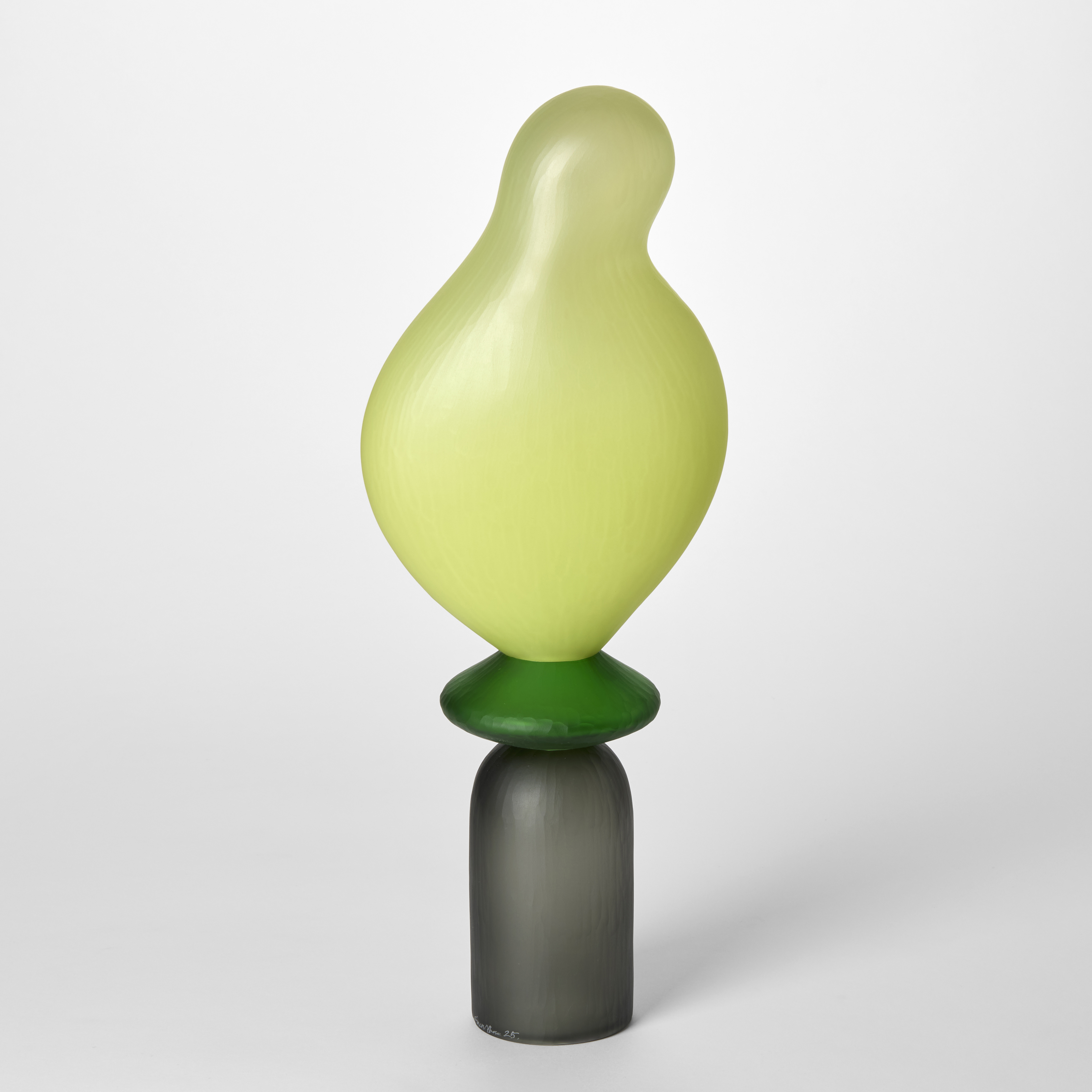tall opaque abstract figurative sculpture created in three sections starting with a bottom grey stemless upside down goblet shape then a round disc in apple green topped with the bright light lime undulating balloon form hand made from blown glass with a repeat cut textured surface