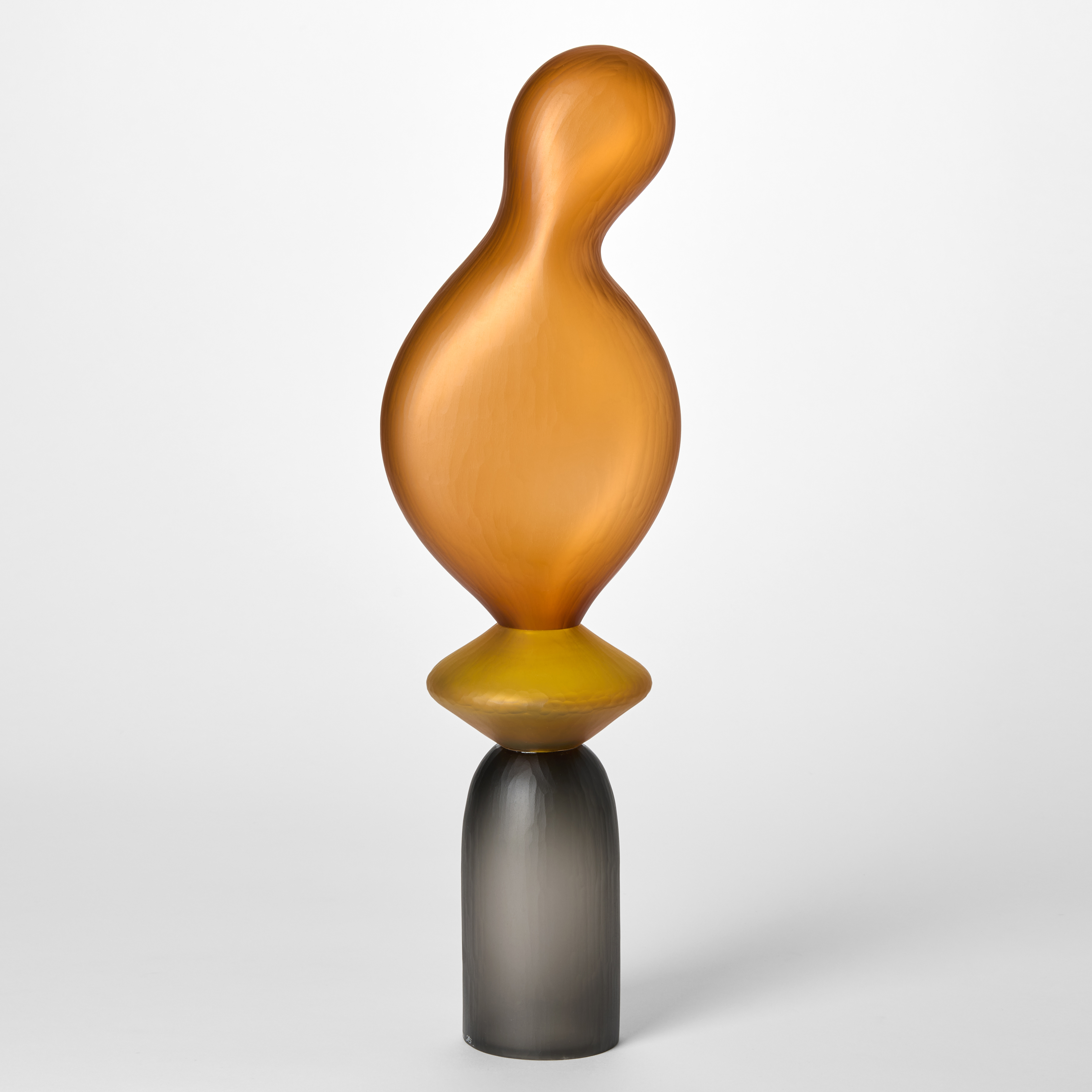 opaque sculpture consisting of stacked forms first an upside down cup in grey then an egg yellow disc topped with an amorphous balloon shape in amber orange hand made from glass with a textured surface