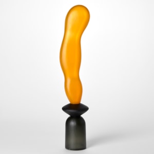tall opaque abstract sculpture created from three balanced forms one on top of the other starting with an upside down grey cup then a disc in black with a long extended orange undulating balloon form on top hand made from blown glass with a textured surface