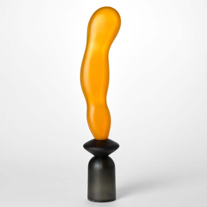 tall opaque abstract sculpture created from three balanced forms one on top of the other starting with an upside down grey cup then a disc in black with a long extended orange undulating balloon form on top hand made from blown glass with a textured surface