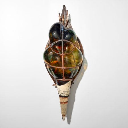 african stylised shield made from a cage created from copper pipe with blown glass in blue green and amber bulging through the gaps strapped with a wooden back board and with a pointed base wrapped in cow hide