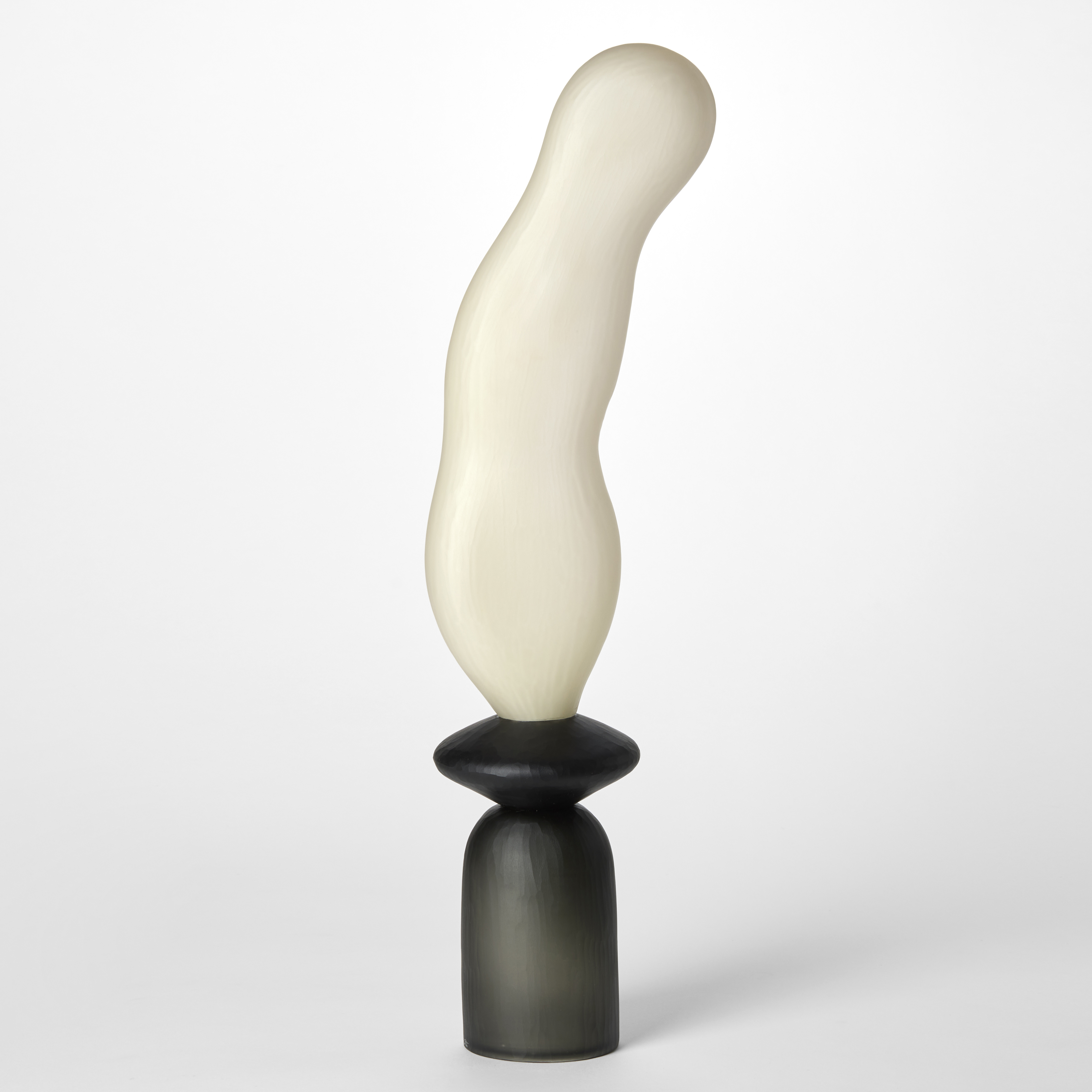 abstract tall opaque sculpture created from two geometric stacked shapes with one in grey and one in black with a long undulating balloon shape perched on the top in alabaster white hand made from blown glass with a textured surface pattern