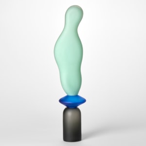 tall opaque sculpture with a textured surface created from three stacked shapes a grey upside down cup a blue disc and a mint long undulating balloon hand blown from glass