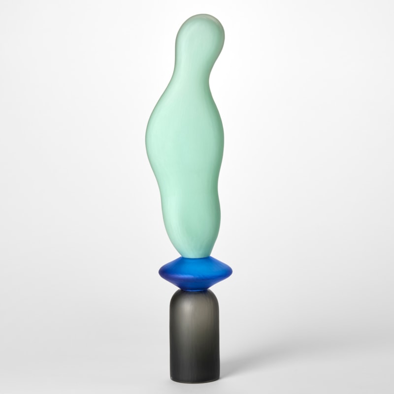 tall opaque sculpture with a textured surface created from three stacked shapes a grey upside down cup a blue disc and a mint long undulating balloon hand blown from glass
