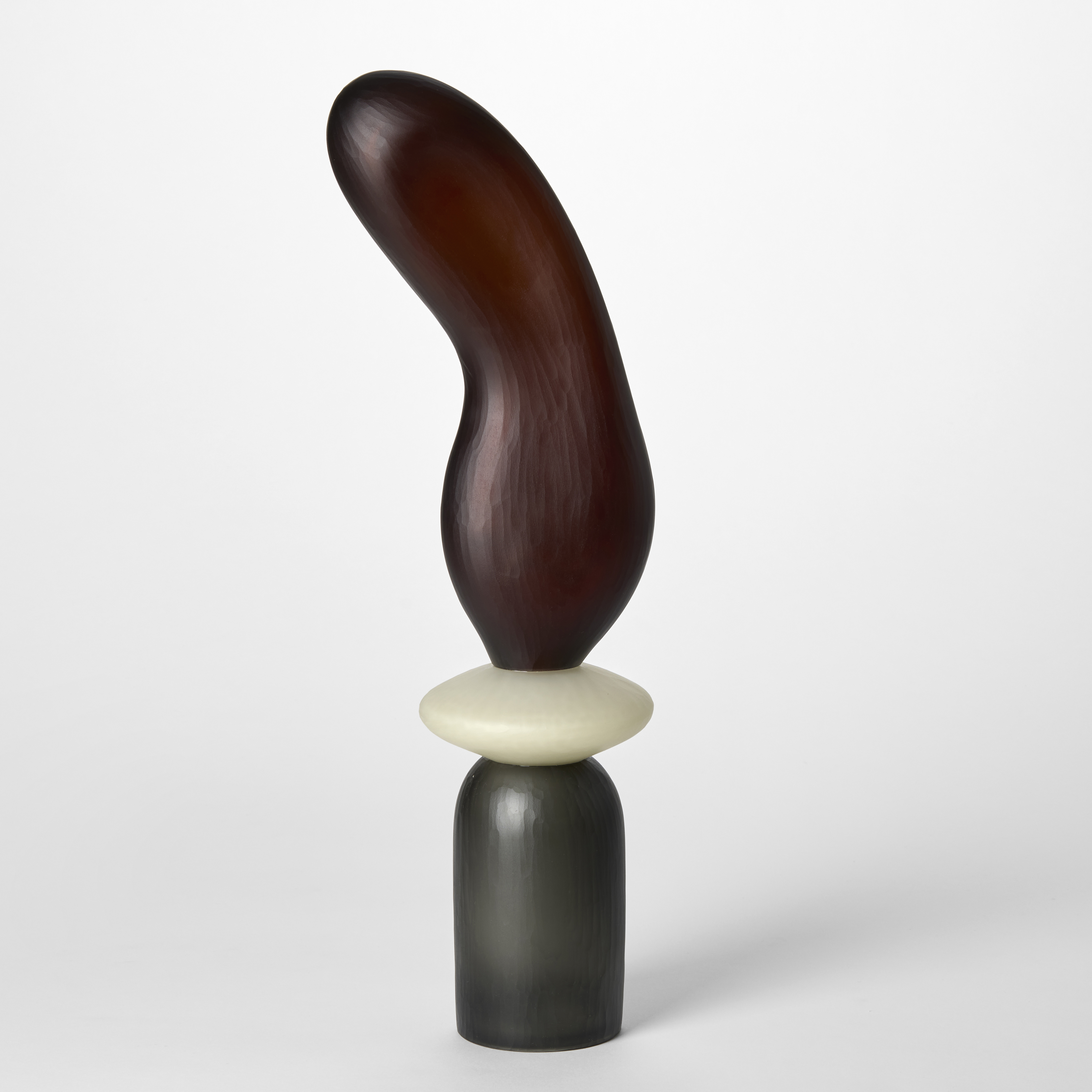 tall abstract semi transparent sculpture consisting of three stacked shapes in grey alabaster white and rich brown hand made from blown glass with a textured surface