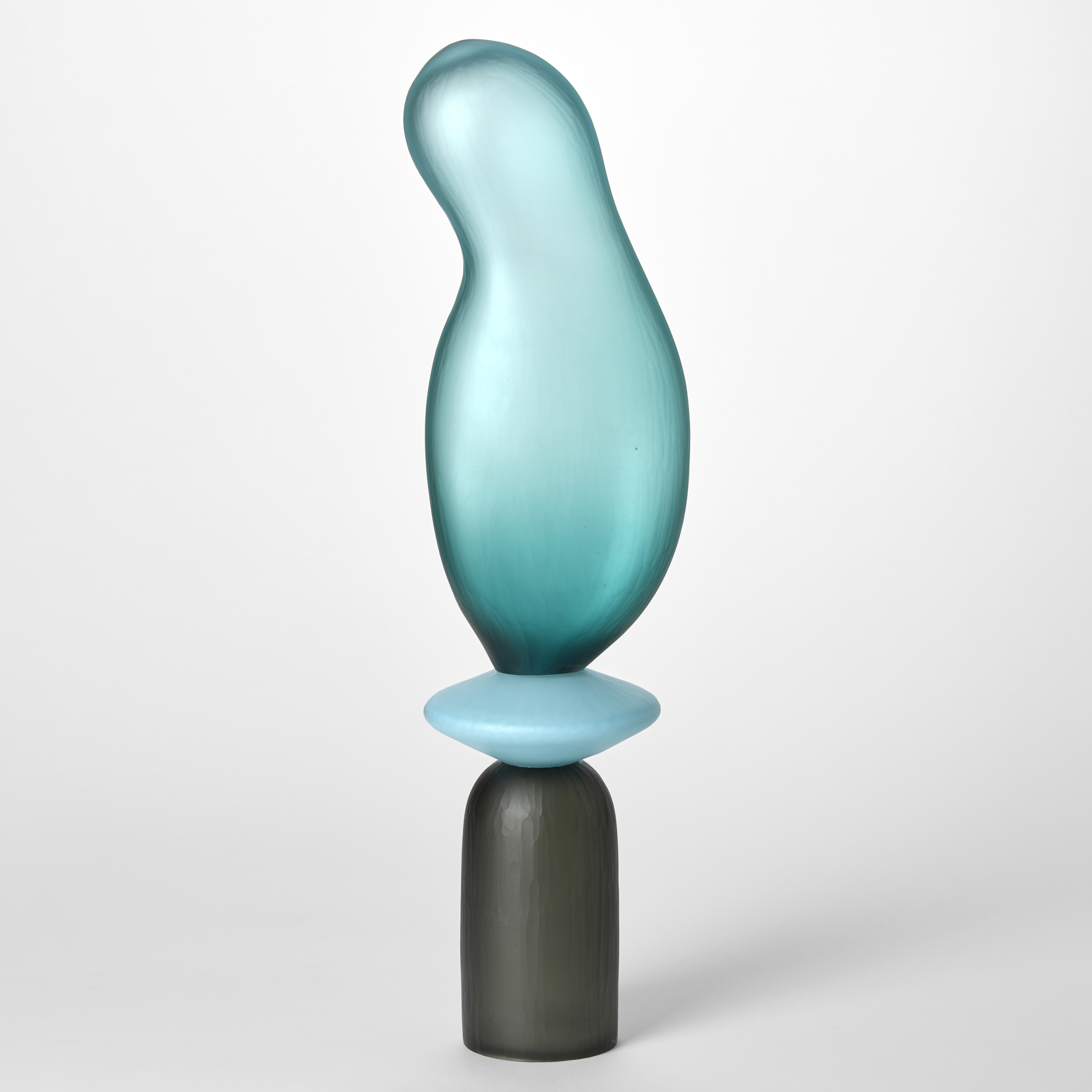 tall opaque sculpture consisting of three stacked shapes an upside down grey cup a turquoise disc and an bulbous balloon form in teal hand blown from glass with a textured surface