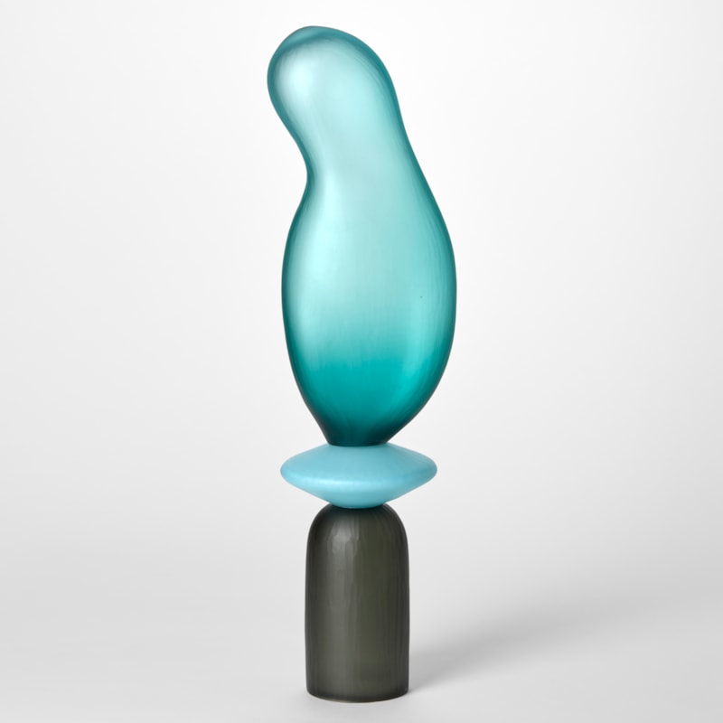 tall opaque sculpture consisting of three stacked shapes an upside down grey cup a turquoise disc and an bulbous balloon form in teal hand blown from glass with a textured surface