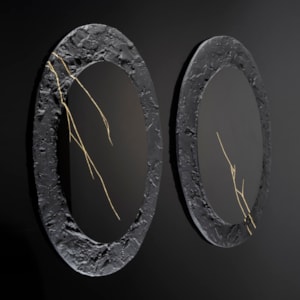 two black wall hung oval discs with thick roughly textured borders and cracks across the surface in gold with central polished black mirrors
