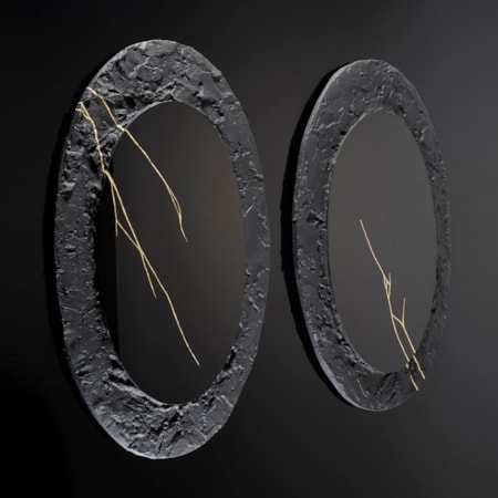two black wall hung oval discs with thick roughly textured borders and cracks across the surface in gold with central polished black mirrors