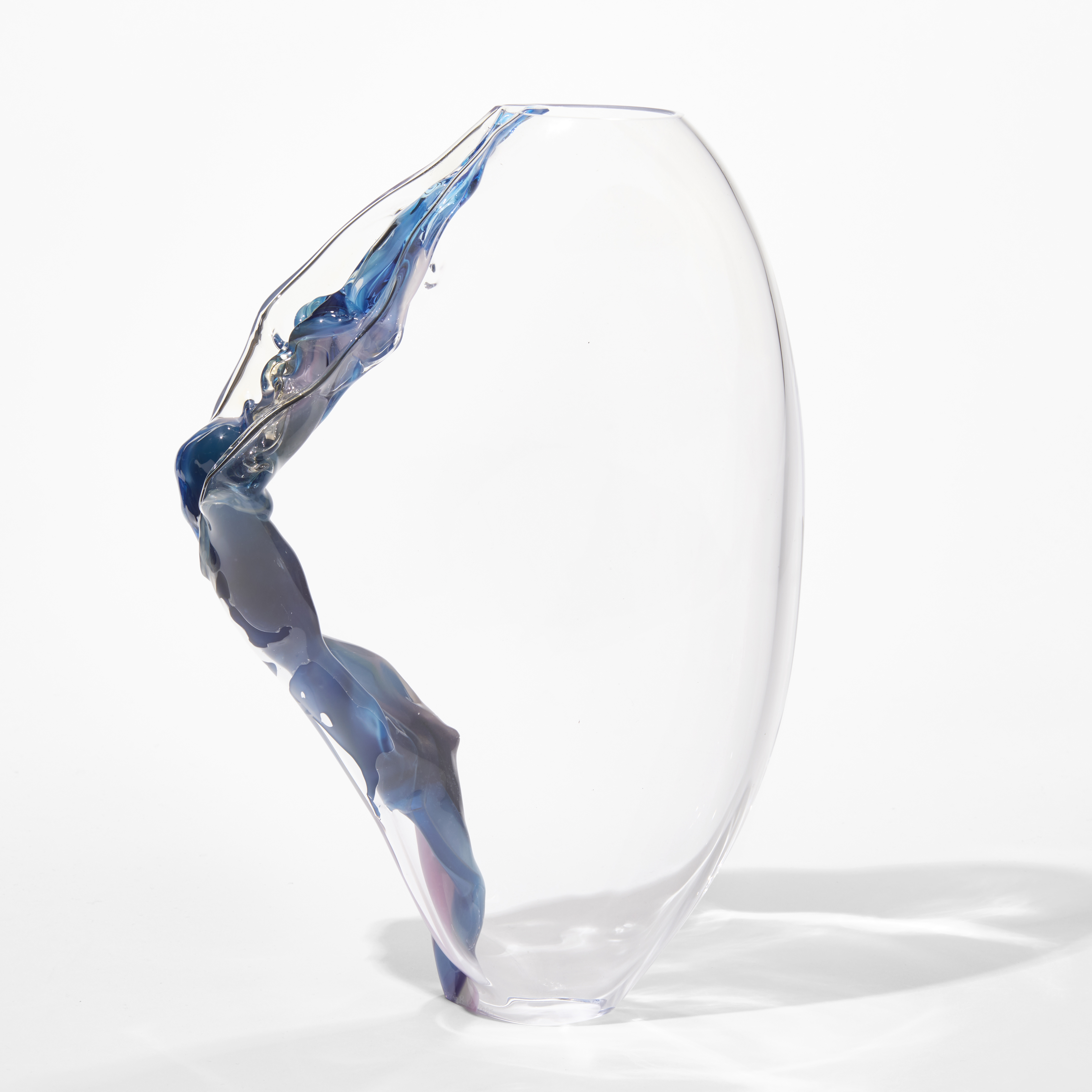 clear standing form with two small openings at the top and bottom with one side curved and rounded the other pointed with an embedded line of flowing colours like a stream of bubbling water in blues pinks and aubergine hand blown from glass