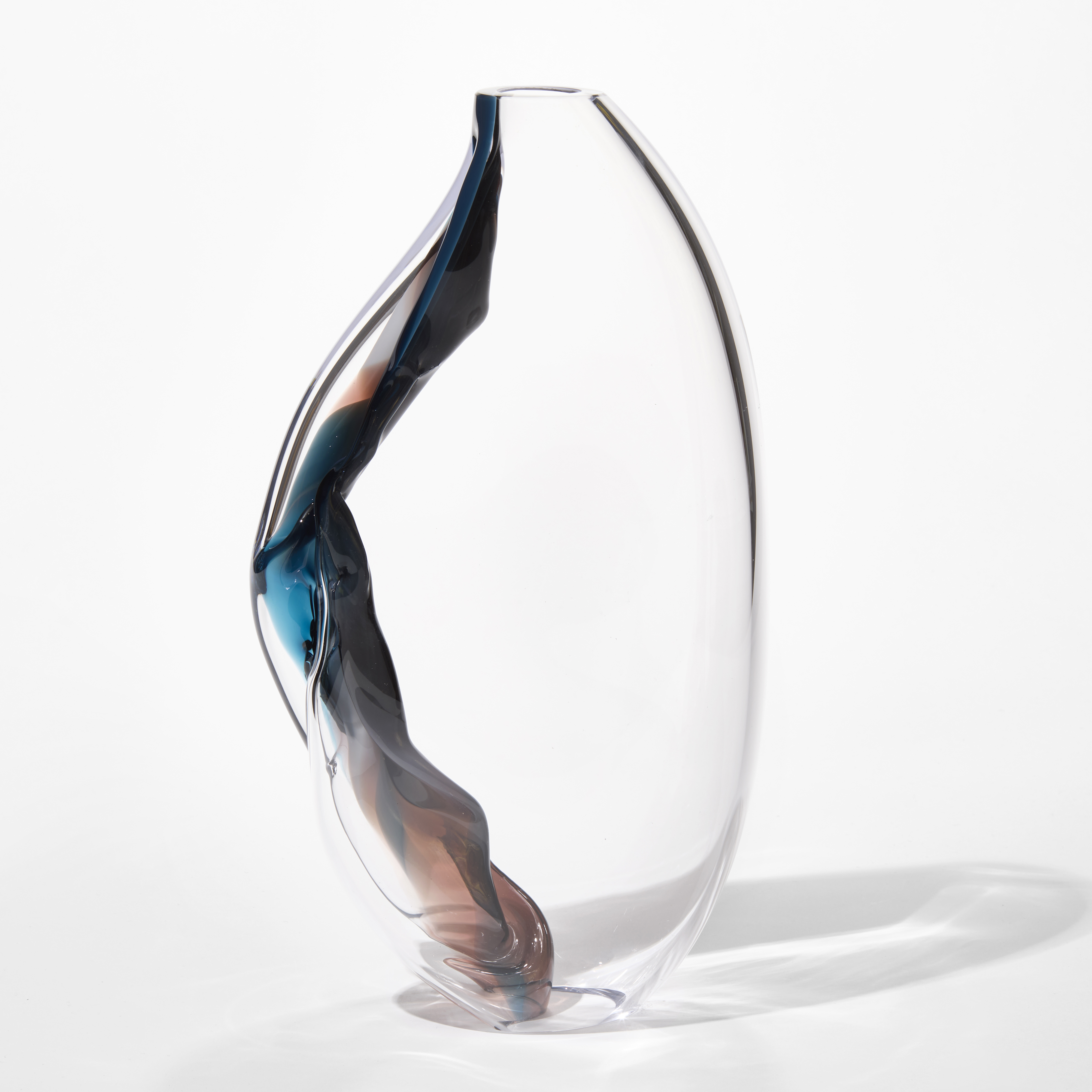 standing clear form narrowing at the top and the base each to small openings with one side bare and curved the other bulging with a cascade of ribboned colour flowing from the top to the bottom following the contour of the form in blues rich pinks and indigo hand made from blown glass