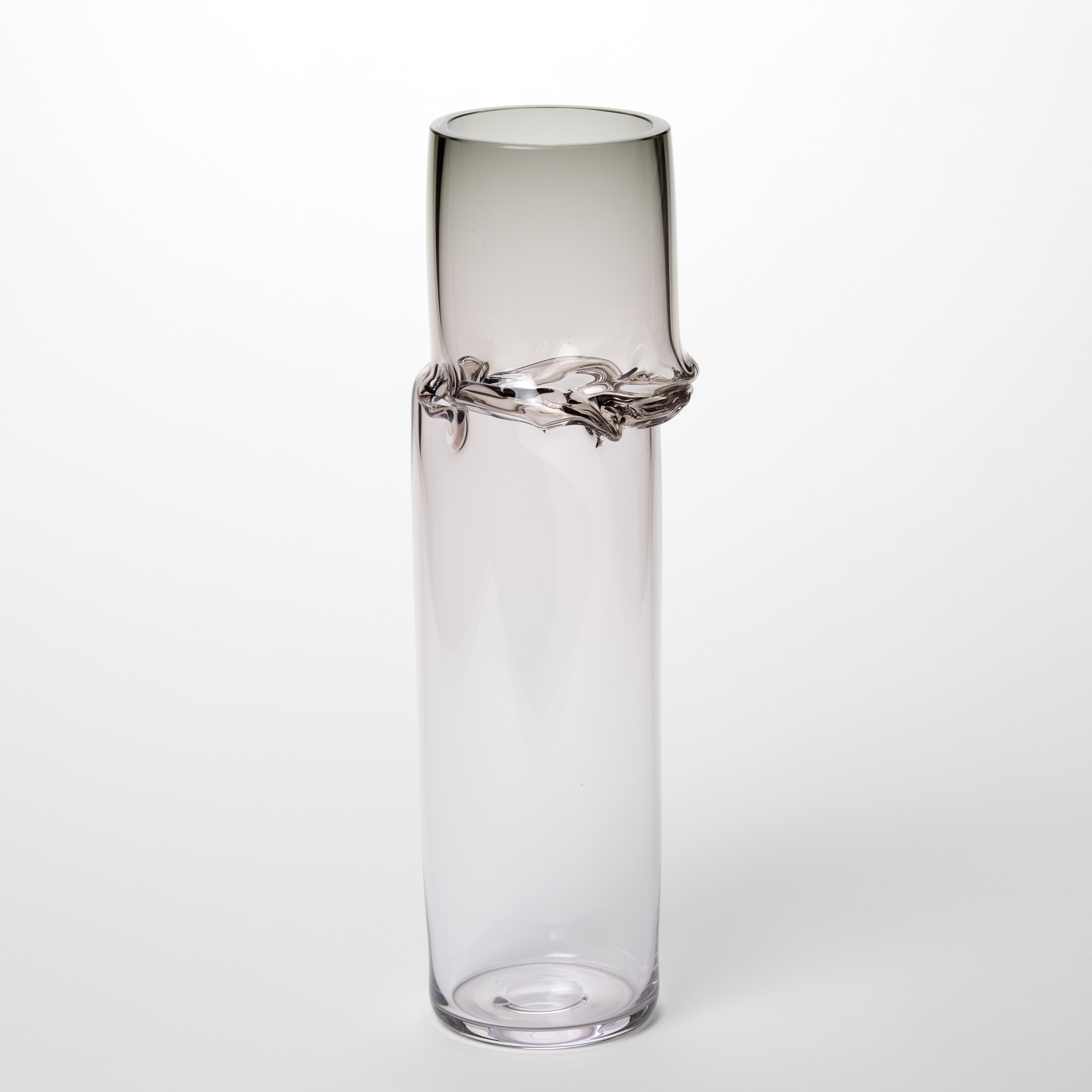 tall transparent tubular vessel with a soft grey top fading to a clear base and an off set creased section a third from the top hand made from glass