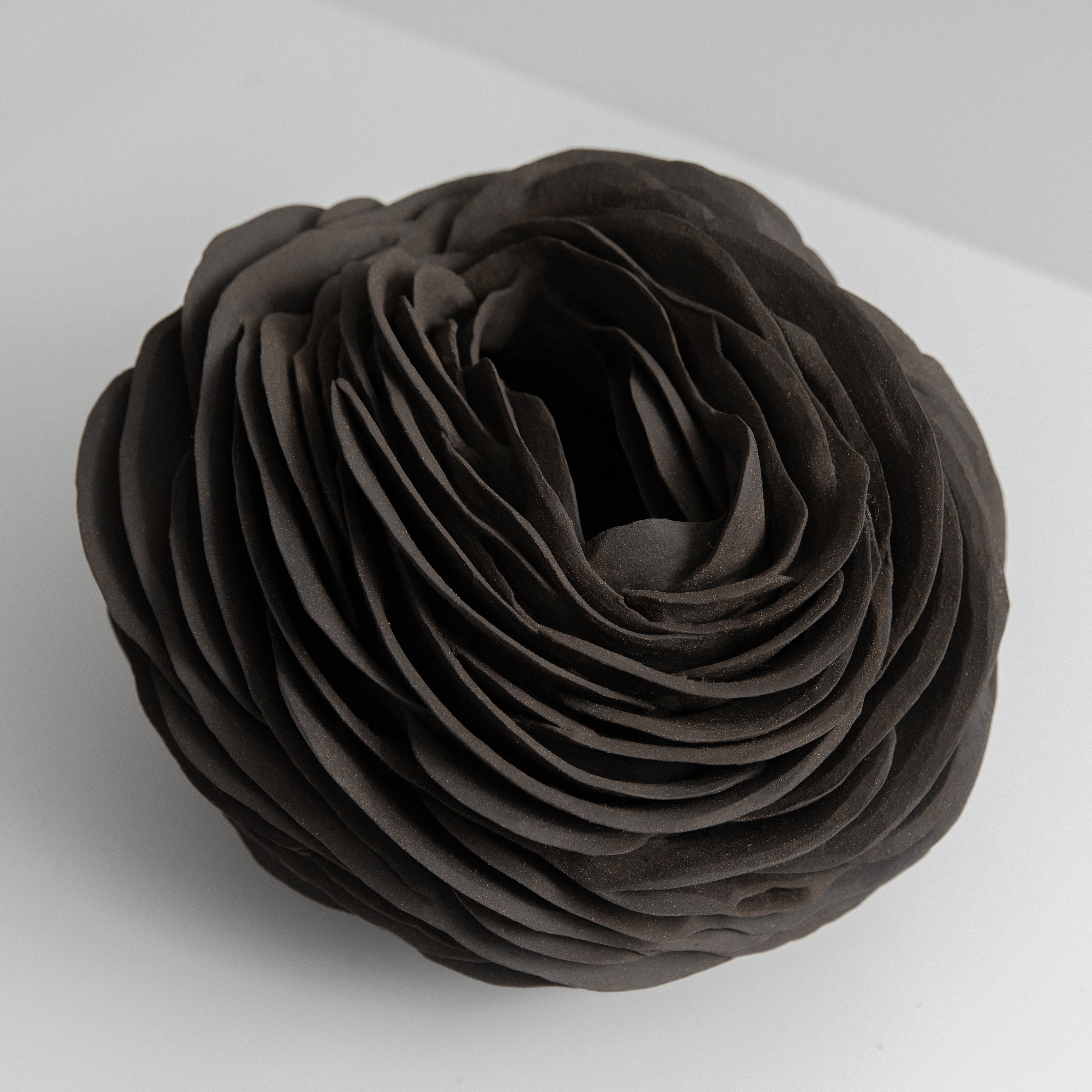 round organic vessel with slit top opening and the entire shape covered in curved interwoven shards hand made from black stoneware