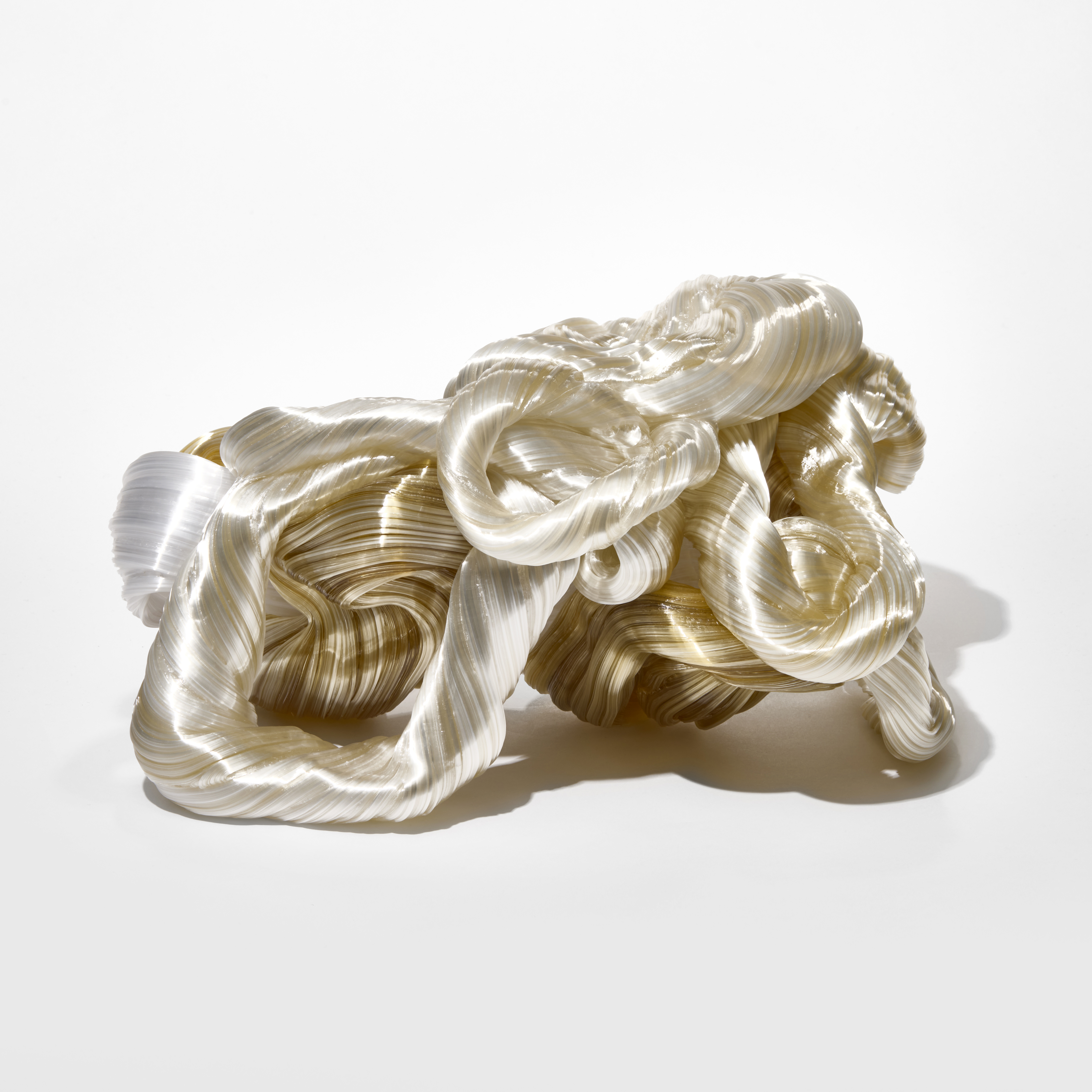 stacked low glistening mass of intertwined ridged glossy looping ropes in amber soft gold and white hand made from sculpted glass
