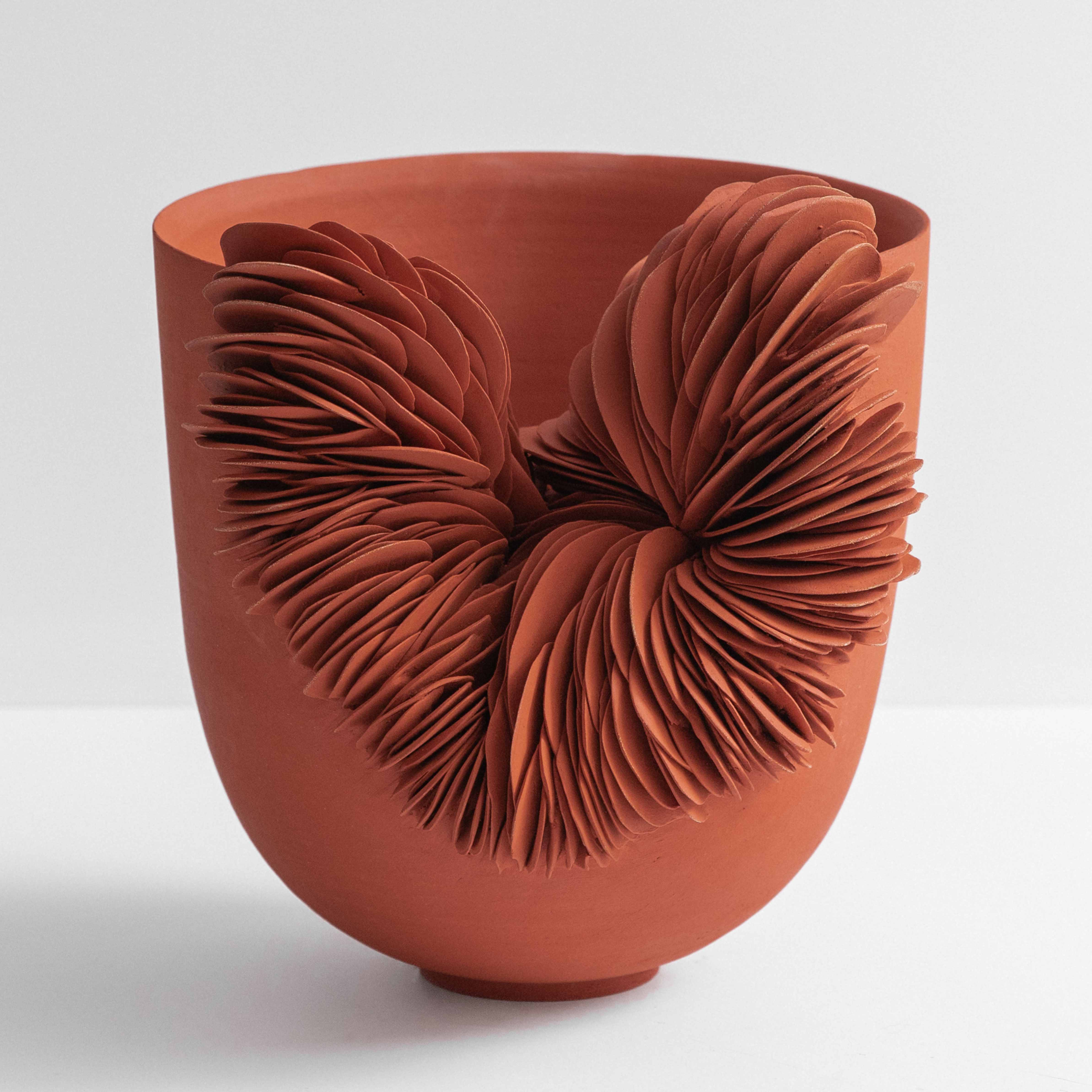 rich rust coloured round thrown bowl with slightly flaring sides and the front section cut away and the gap filled with stacked shards hand made from terracotta
