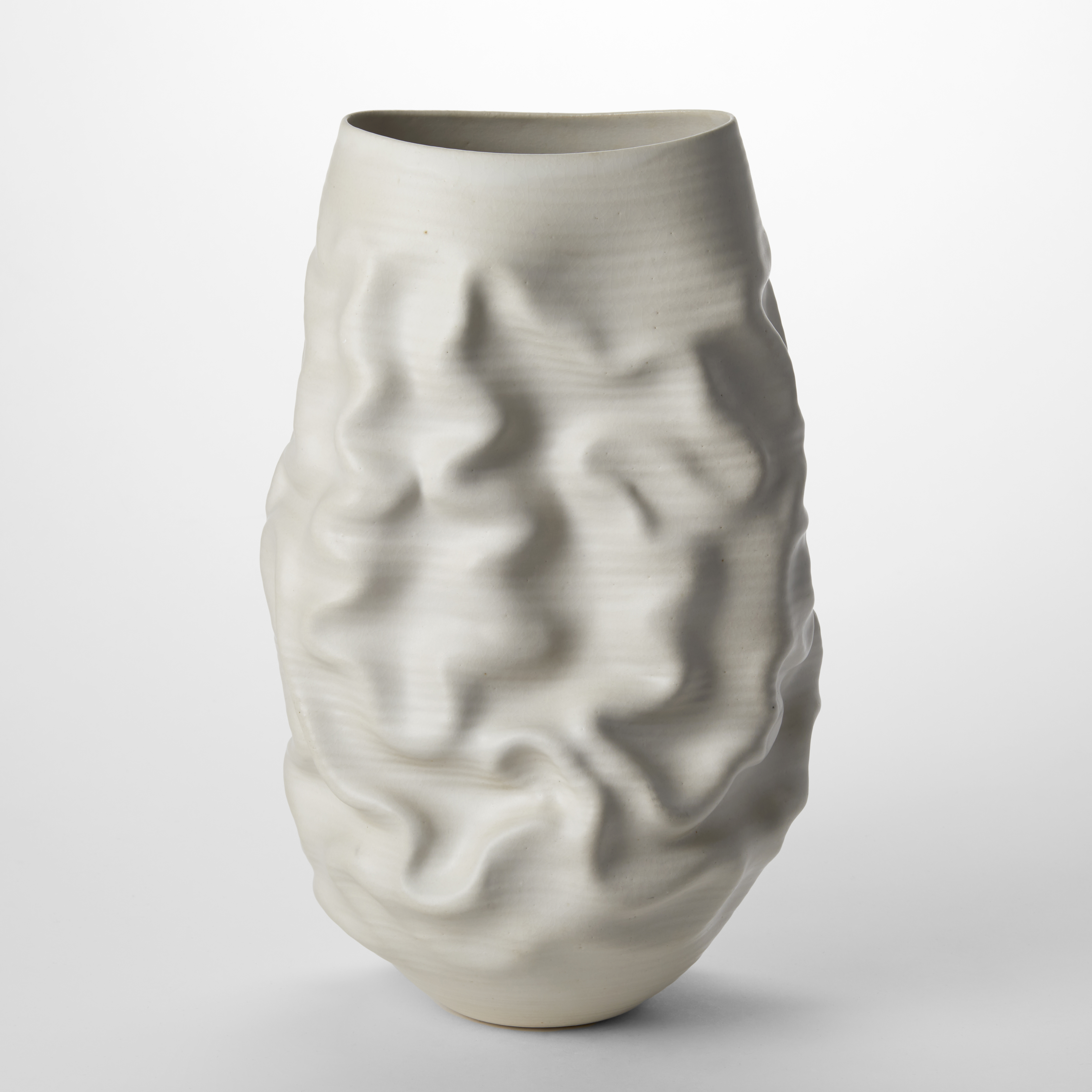 tall white ovoid sculptural vessel with the top cut off to a sweeping wide oval opening with soft undulations and creases across the surface hand made from thrown clay