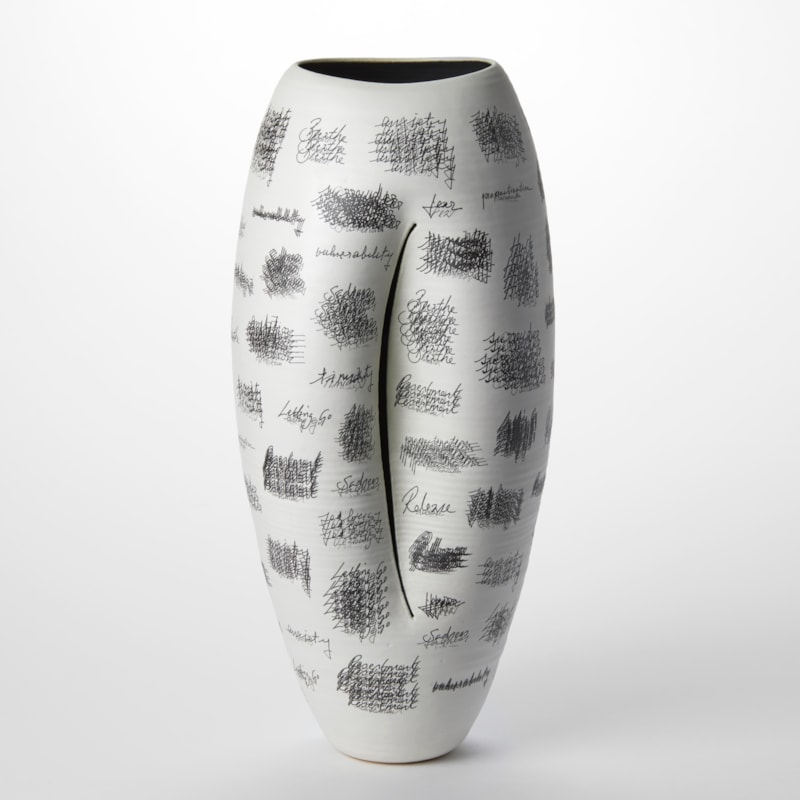 tall white oval vessel with curved slit on the front and a black interior with the surface covered in repeated lines of black hand writing hand made from clay