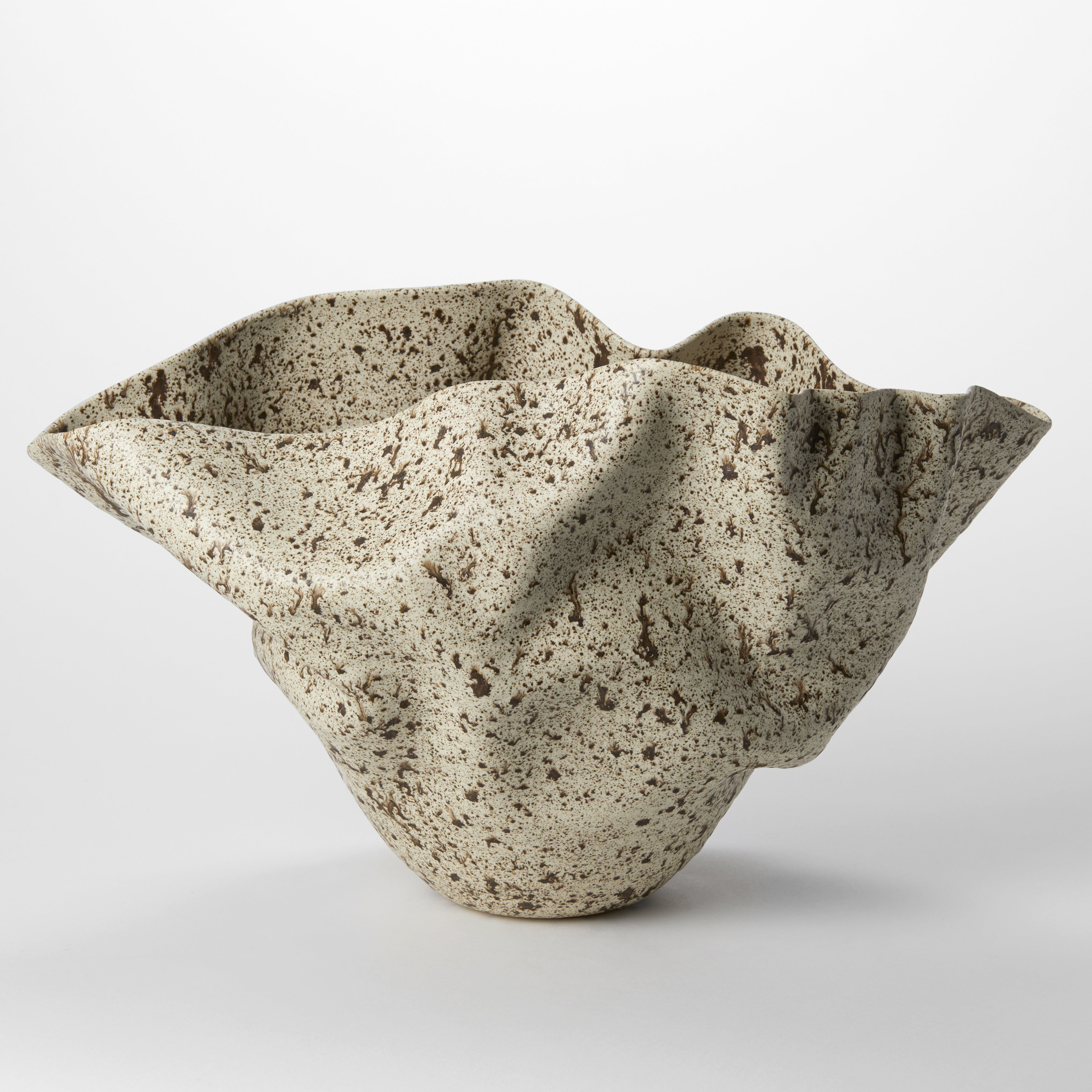 wide flaring undulating rimmed centrepiece narrowing to a small base with soft wrinkles on the surface in a light taupe colour with dark brown plats all over the surface hand thrown from clay