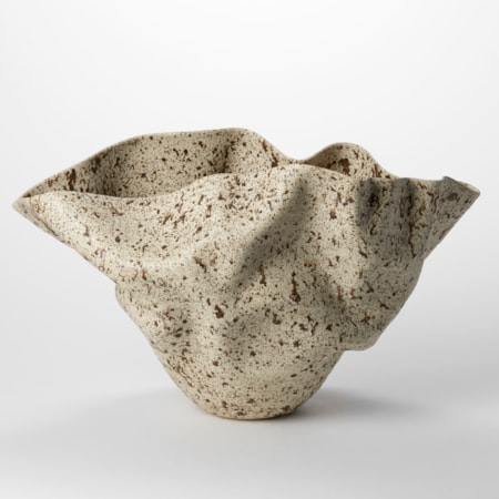wide flaring undulating rimmed centrepiece narrowing to a small base with soft wrinkles on the surface in a light taupe colour with dark brown plats all over the surface hand thrown from clay
