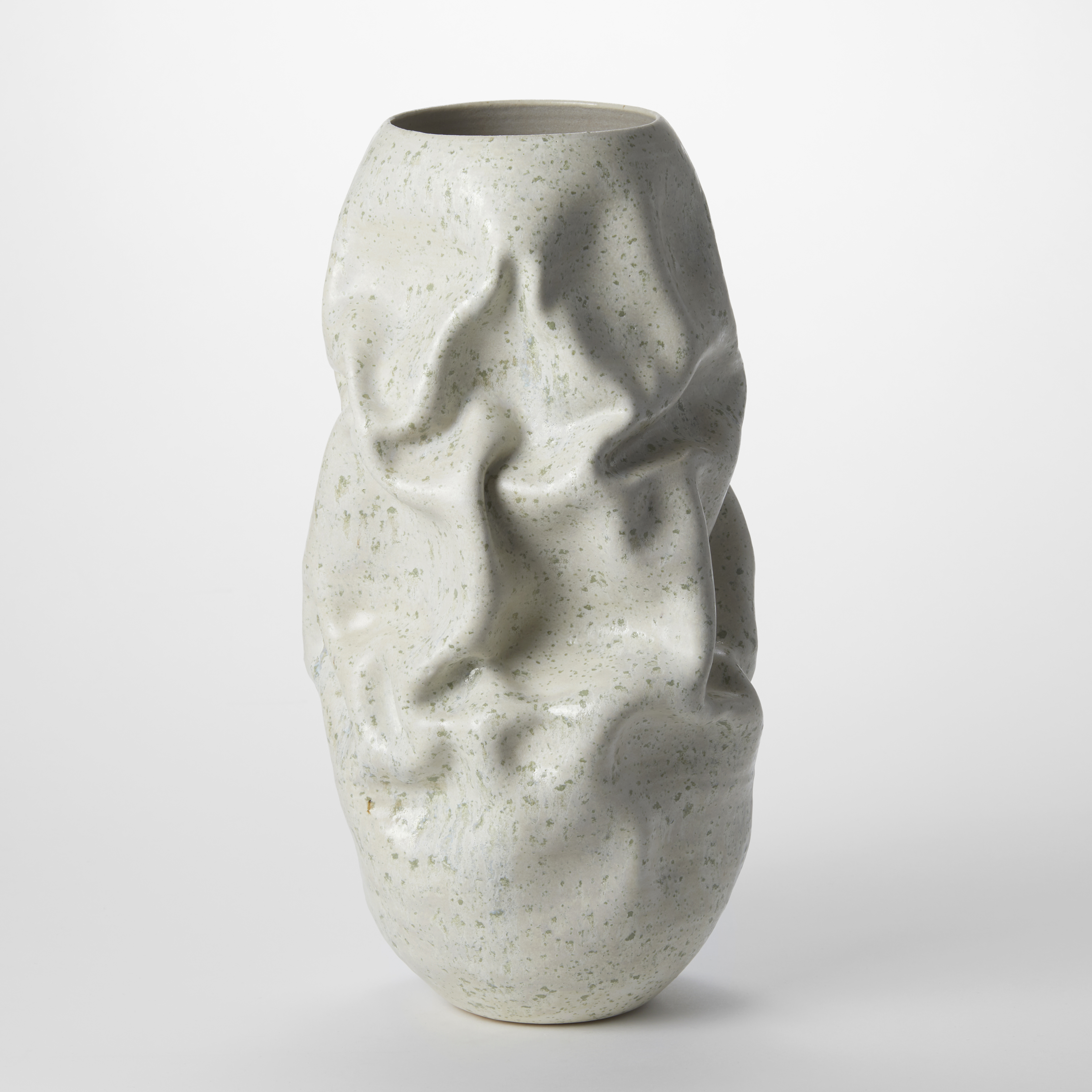 tall soft cylindrical ceramic vessel with a soft white exterior and light olive green speckles with the appearance of terrazzo tiles patterns with soft large creases within the form hand made from clay
