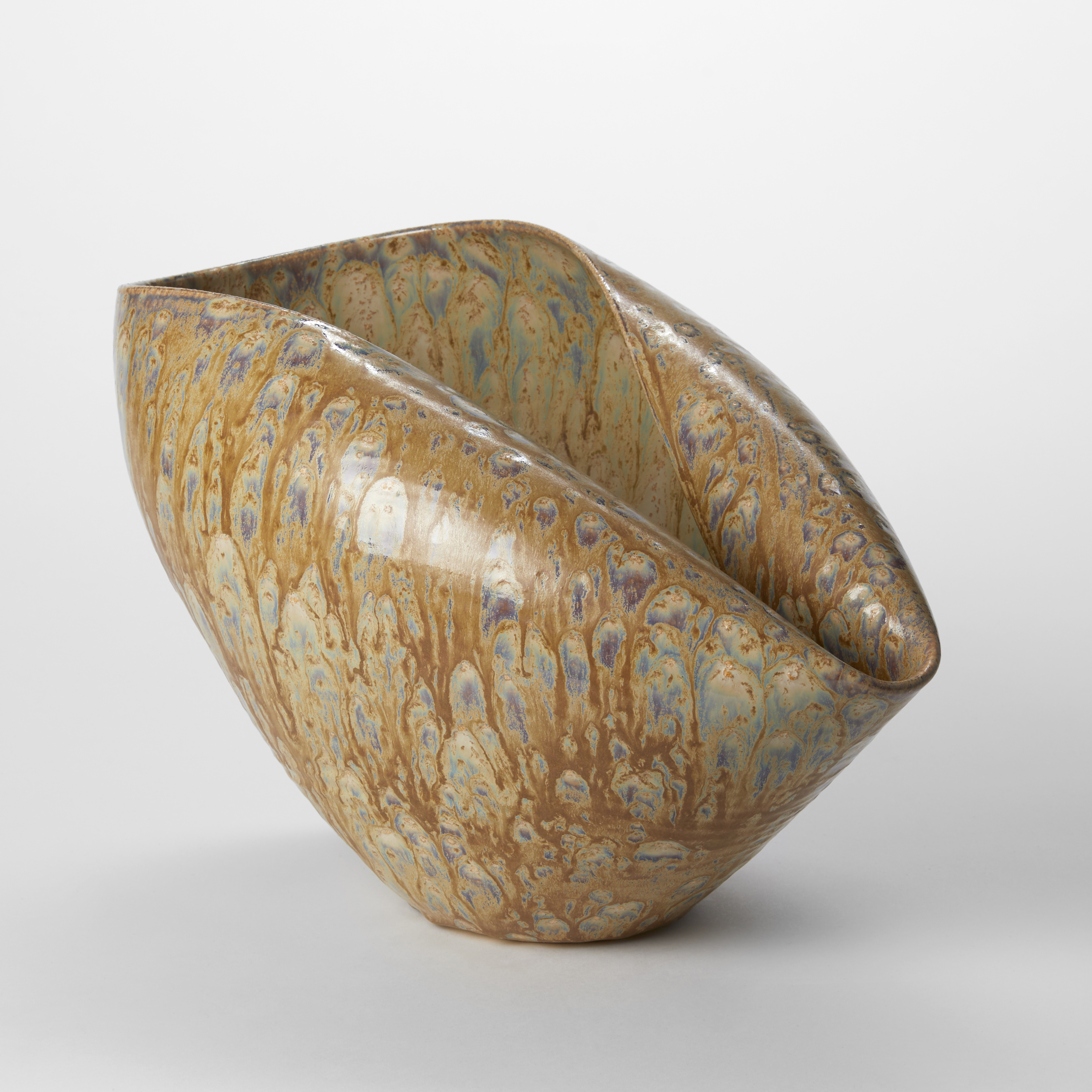 abstract shell like centrepiece created from a thrown bowl with inverted folded in rim on one side with a dripping glaze all over the surface in ochre grey brown and blue hand made from clay 