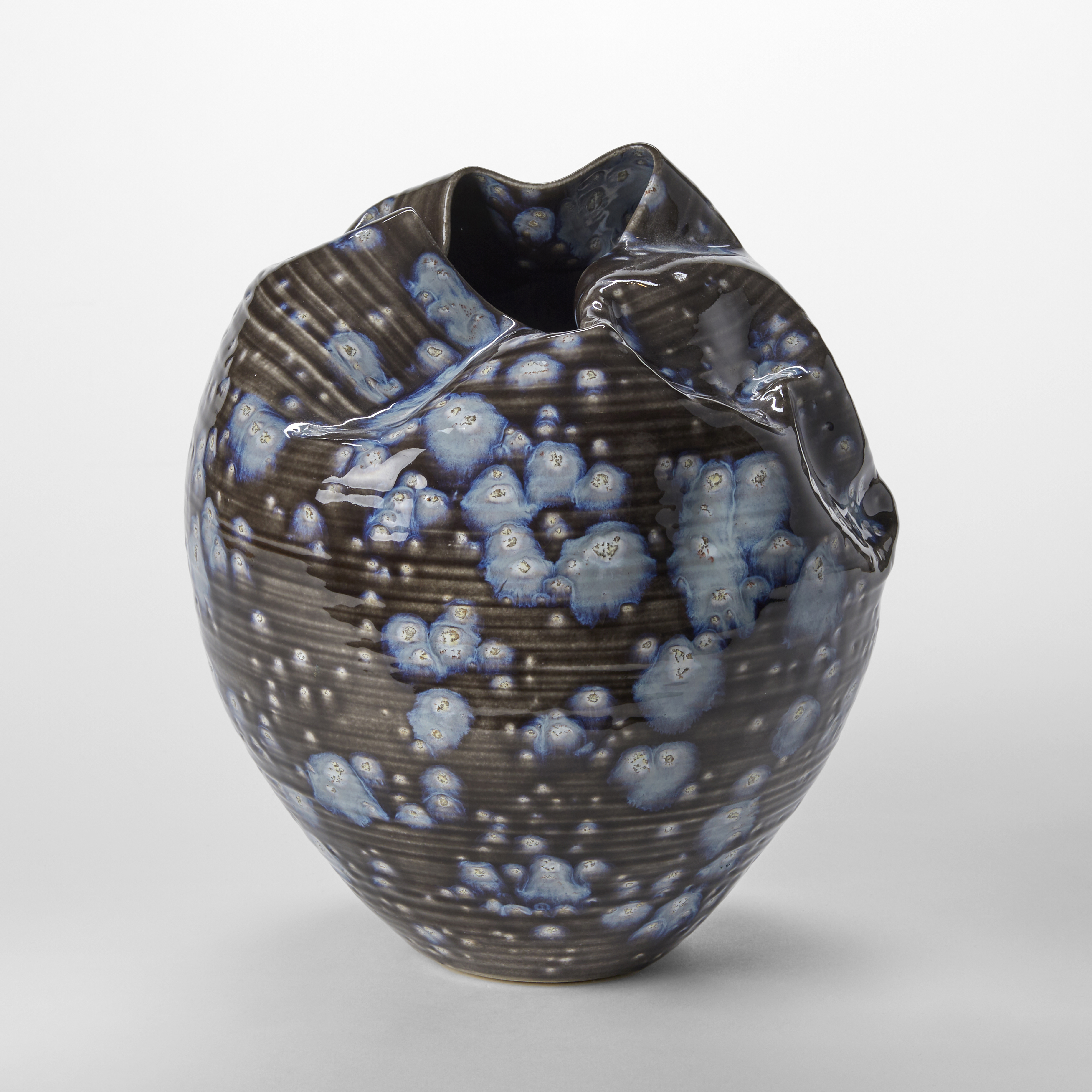 black small round sculptural vessel with creased and gathered top opening with blue exploding splodges all over the surface hand thrown from clay