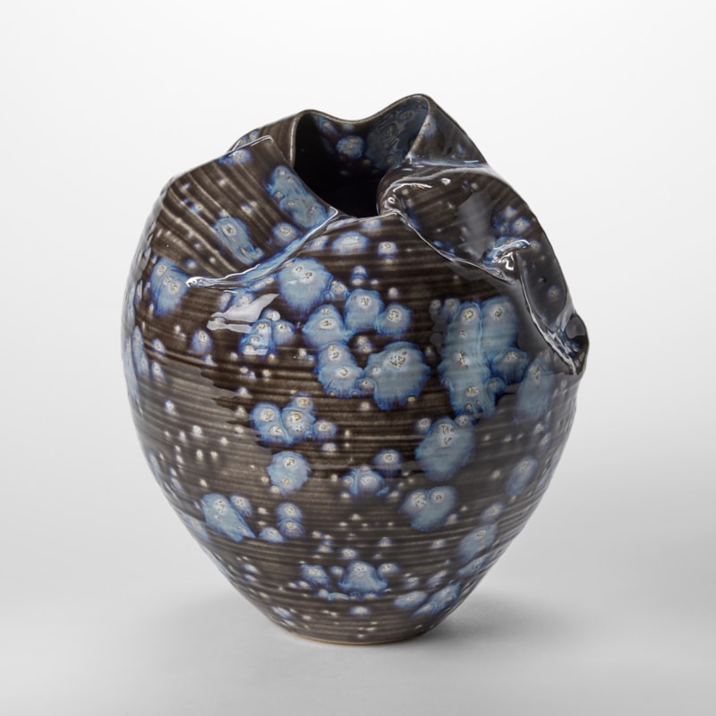 black small round sculptural vessel with creased and gathered top opening with blue exploding splodges all over the surface hand thrown from clay
