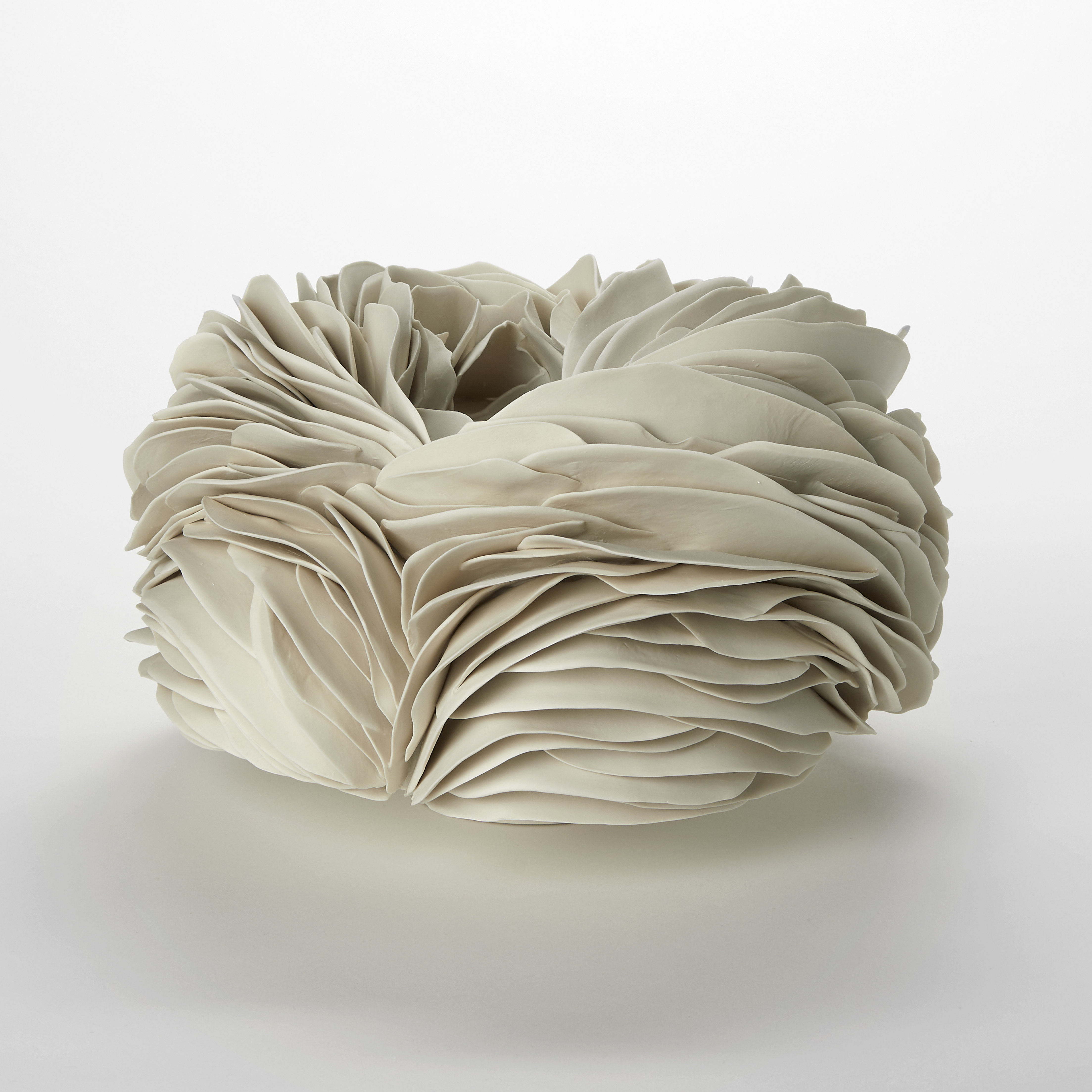 alabaster cream round nest shaped sculpture with a small top opening created from long stacked organic thin undulating layers which following around shape hand made from porcelain