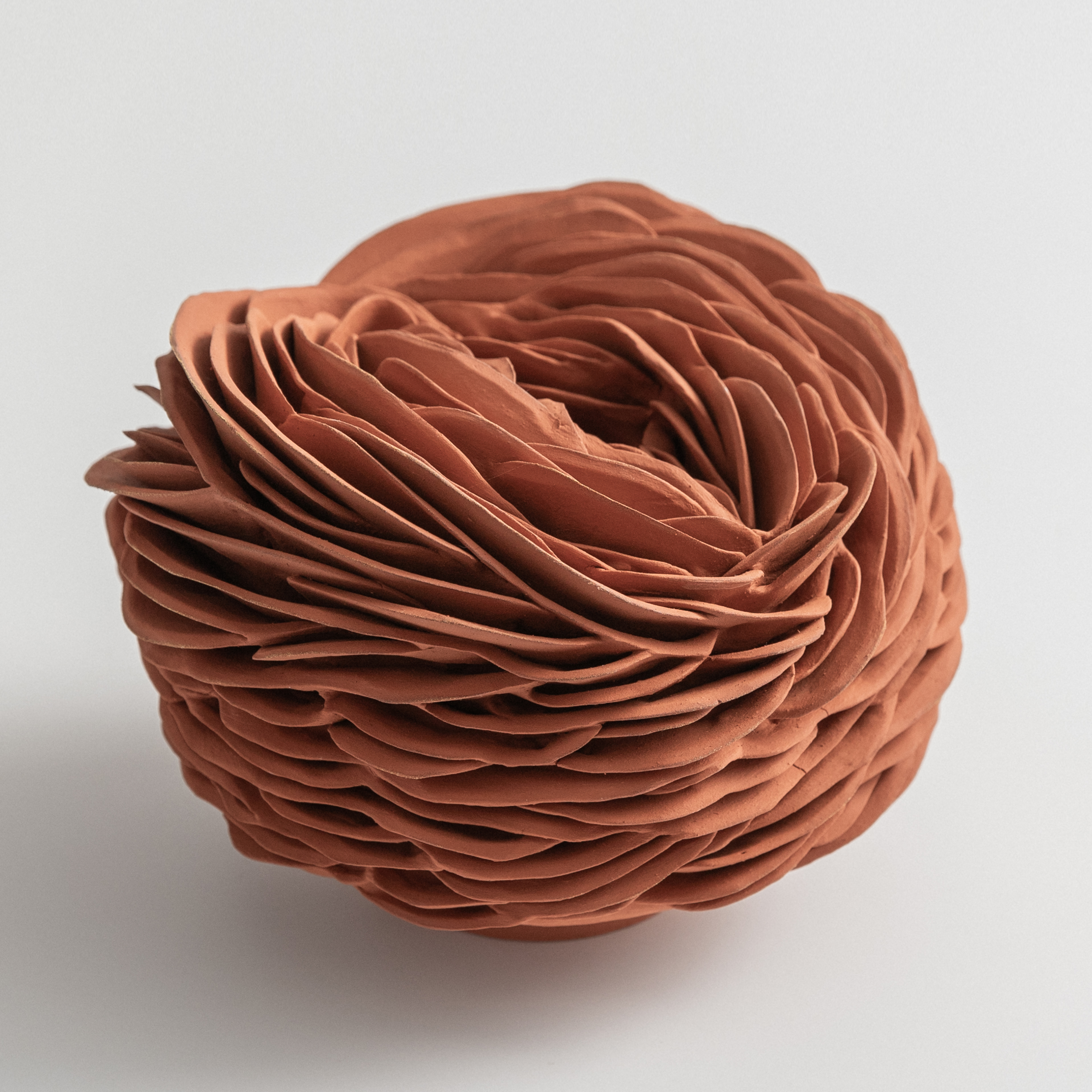 low round rust coloured nest like form with a narrow top opening and the entire surface covered in interlocking curved shards hand made from terracotta