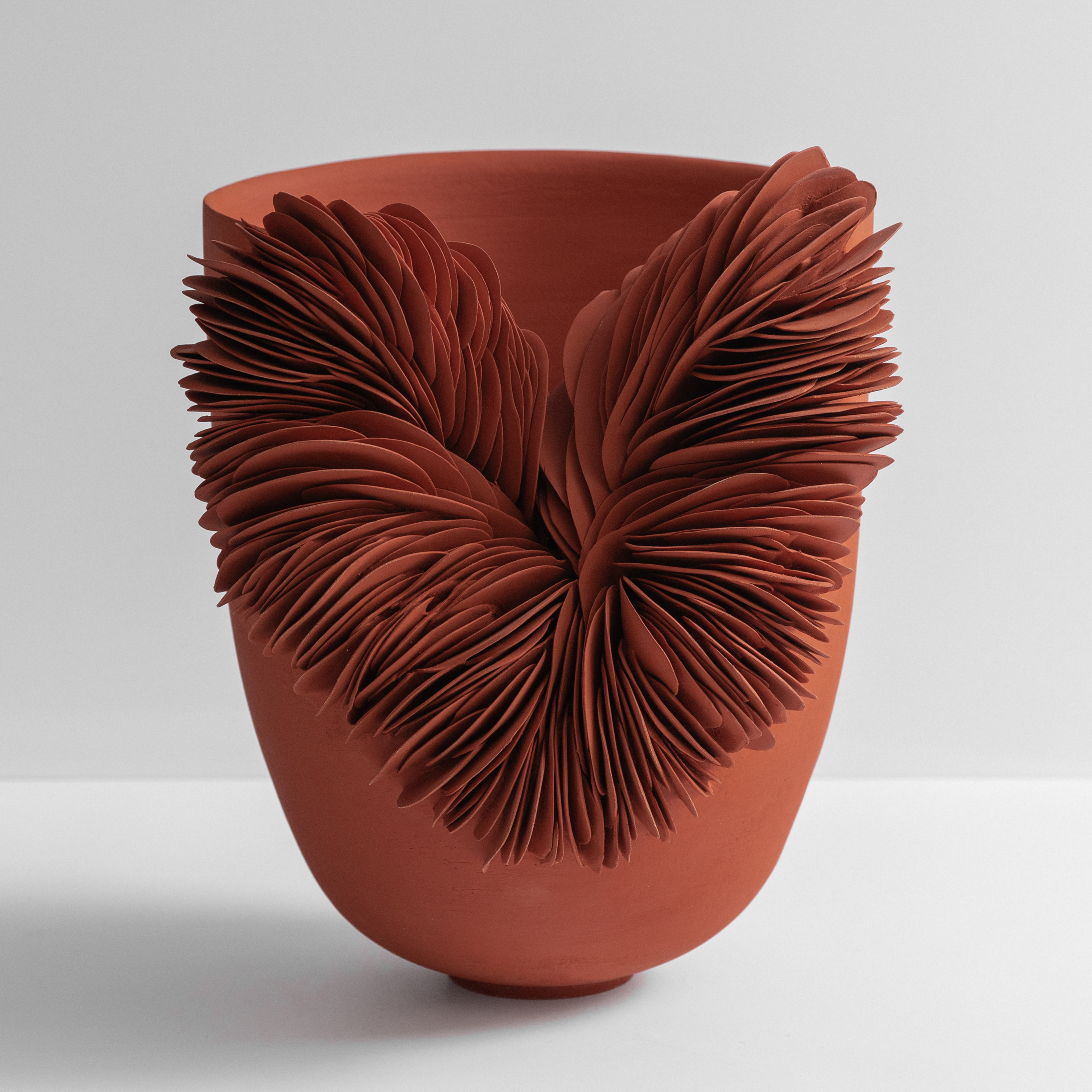 tall widening rust coloured thrown vessel with a third section cut away and the gap filled with stacked shards hand made from terracotta