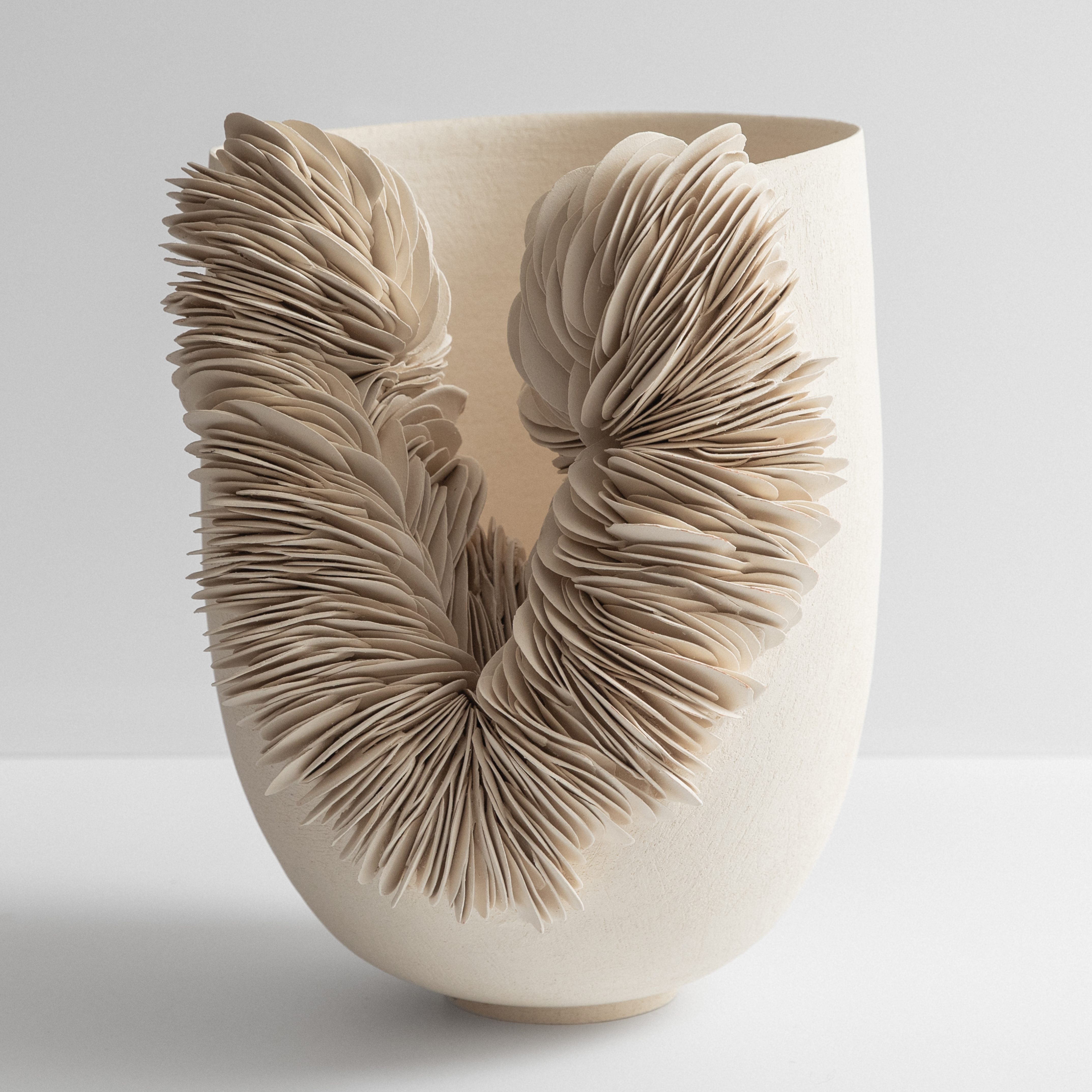 tall off white vessel with the front section cut away and filled with stacked shards hand thrown and made from stoneware clay