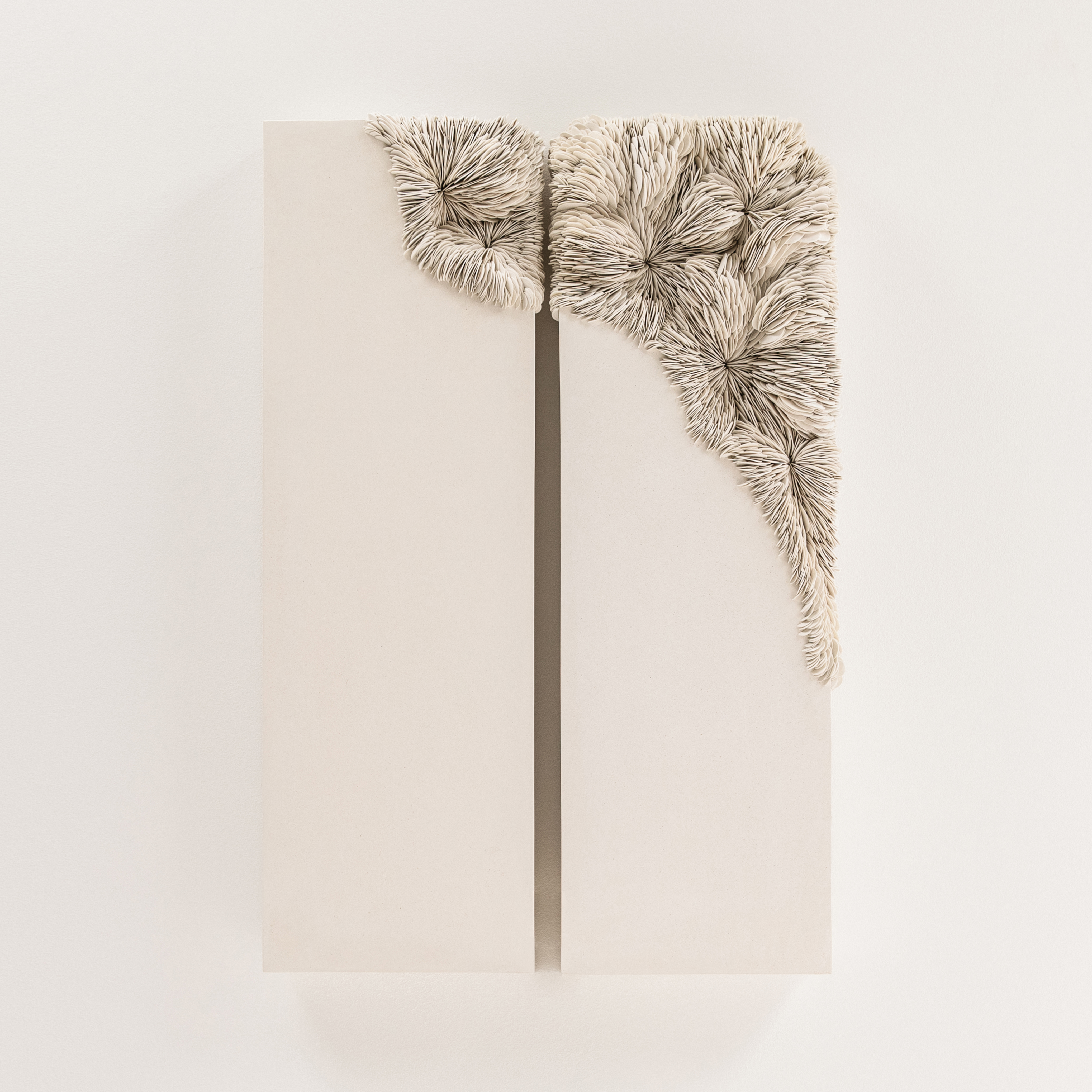 wall hanging sculptural artwork consisting of two vertical identical chunky white slabs with the upper right hand corners covered in an organic sprawl of stacked shards with the appearance as if growing over the surface hand made from porcelain and tadelakt plaster